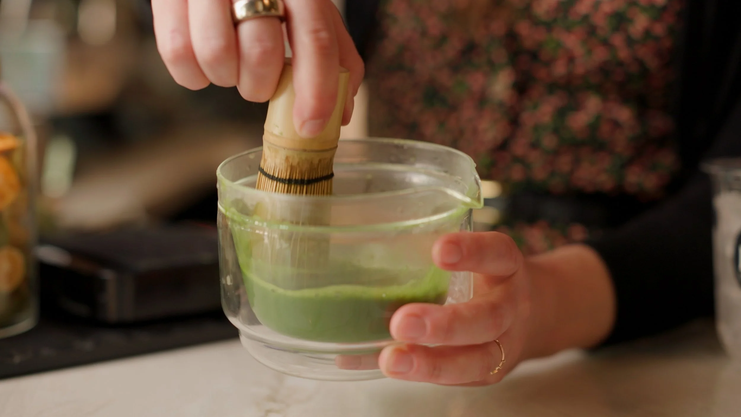 Person holding a glass with a green cocktail and a bamboo cocktail stirrer.