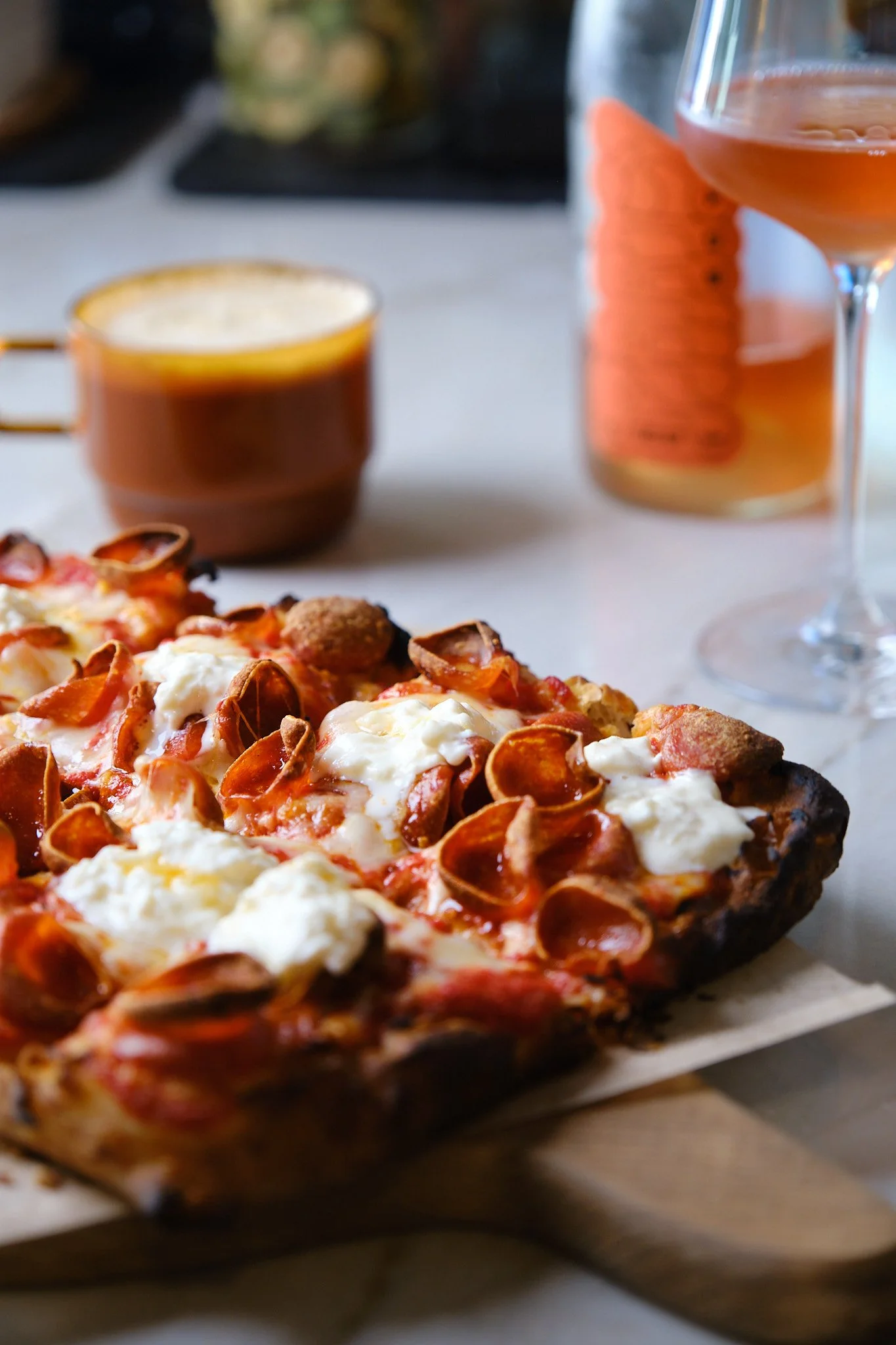 Close-up of a pepperoni pizza with melted cheese and a crispy crust on a wooden tray, with drinks and a blurred background.