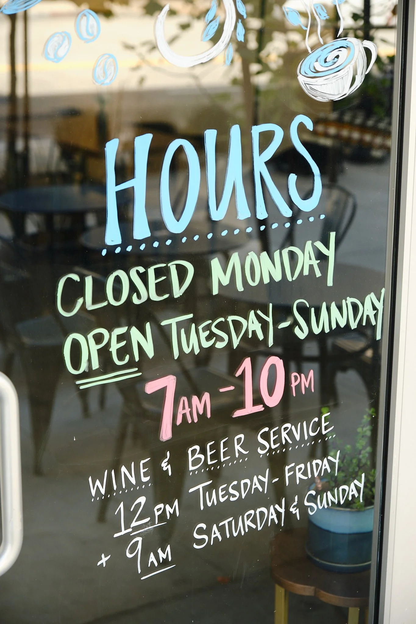 Sign on a window advertising hours of operation, including 7am to 10pm, and mentioning wine, beer, and beverage service from Tuesday through Sunday.