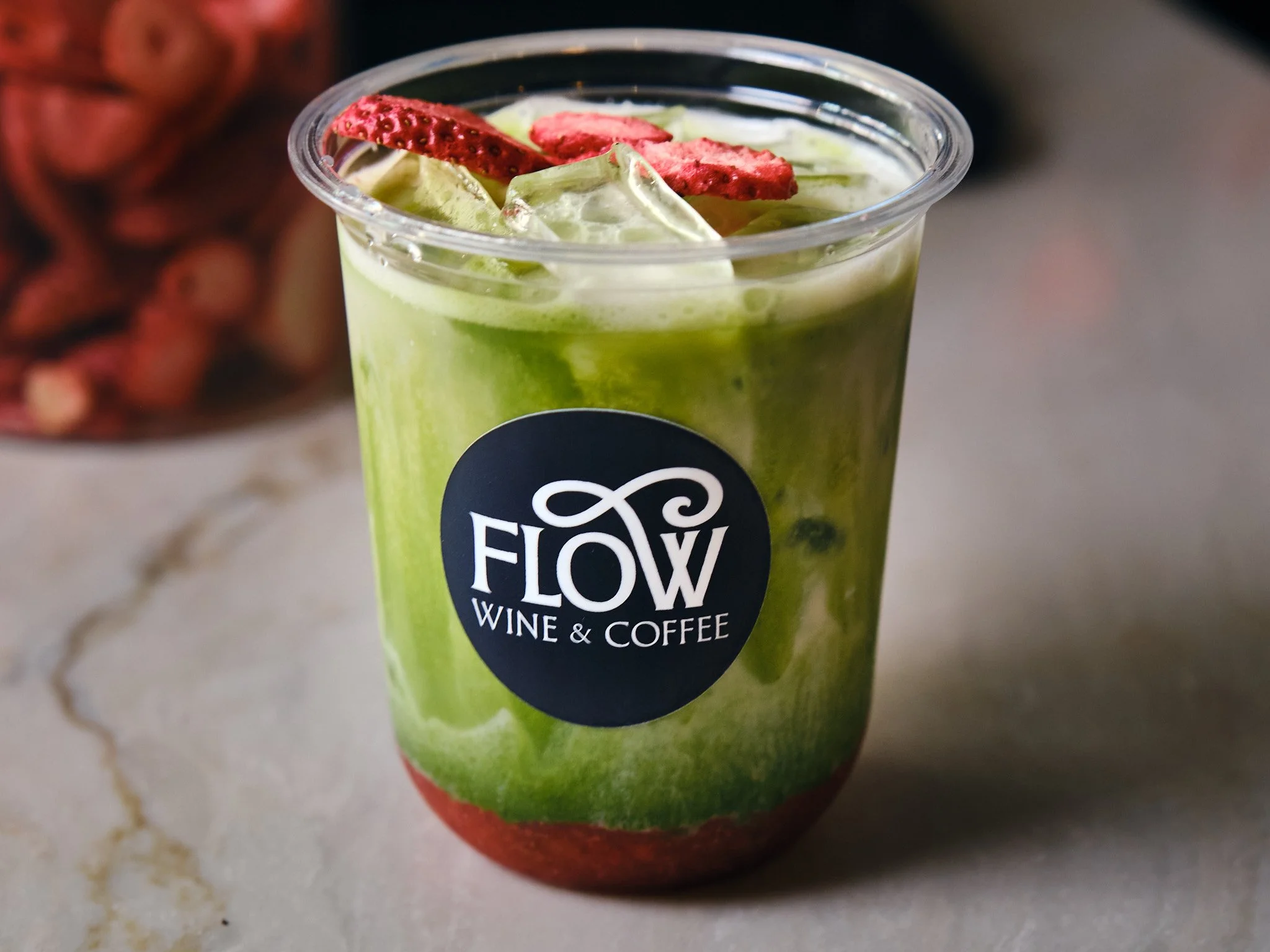 A green smoothie in a plastic cup with ice, topped with sliced strawberries, on a gray surface.