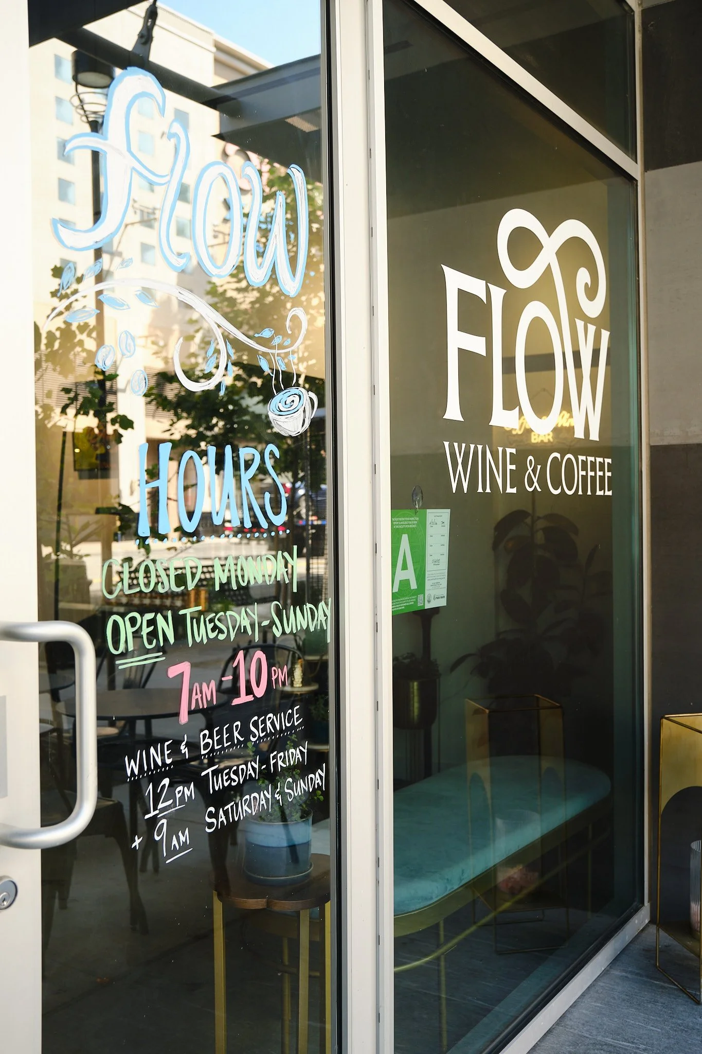 Glass door with restaurant hours and menu items written in colorful chalk, including wine and beer service, and restaurant name 'Flow' with 'Wine & Coffee' included.
