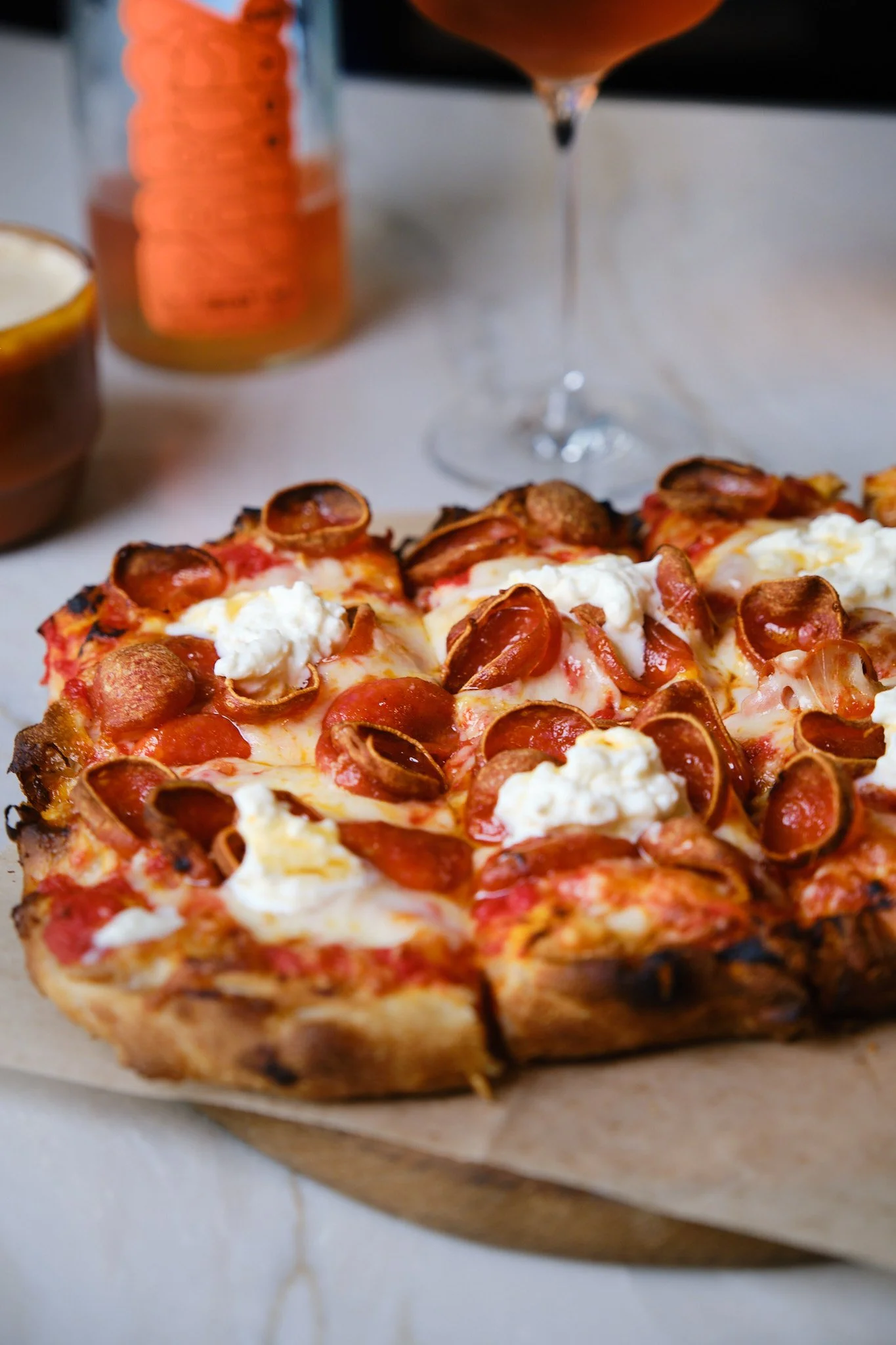 Close-up of a pepperoni and cheese pizza with dollops of ricotta cheese, placed on a piece of parchment paper.