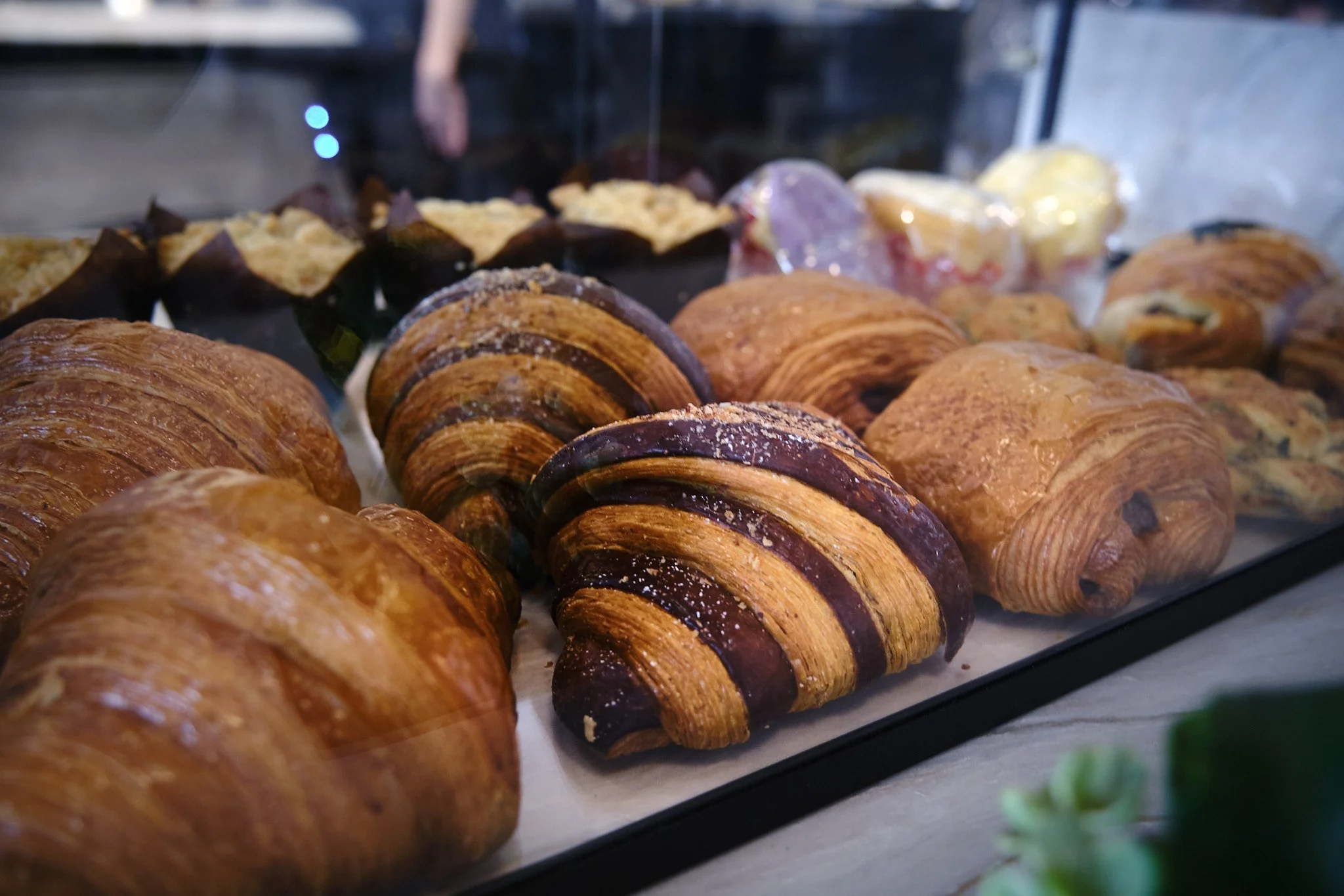Close-up of assorted pastries, including croissants with flaky golden-brown layers and chocolate-topped pastries on a baking tray.