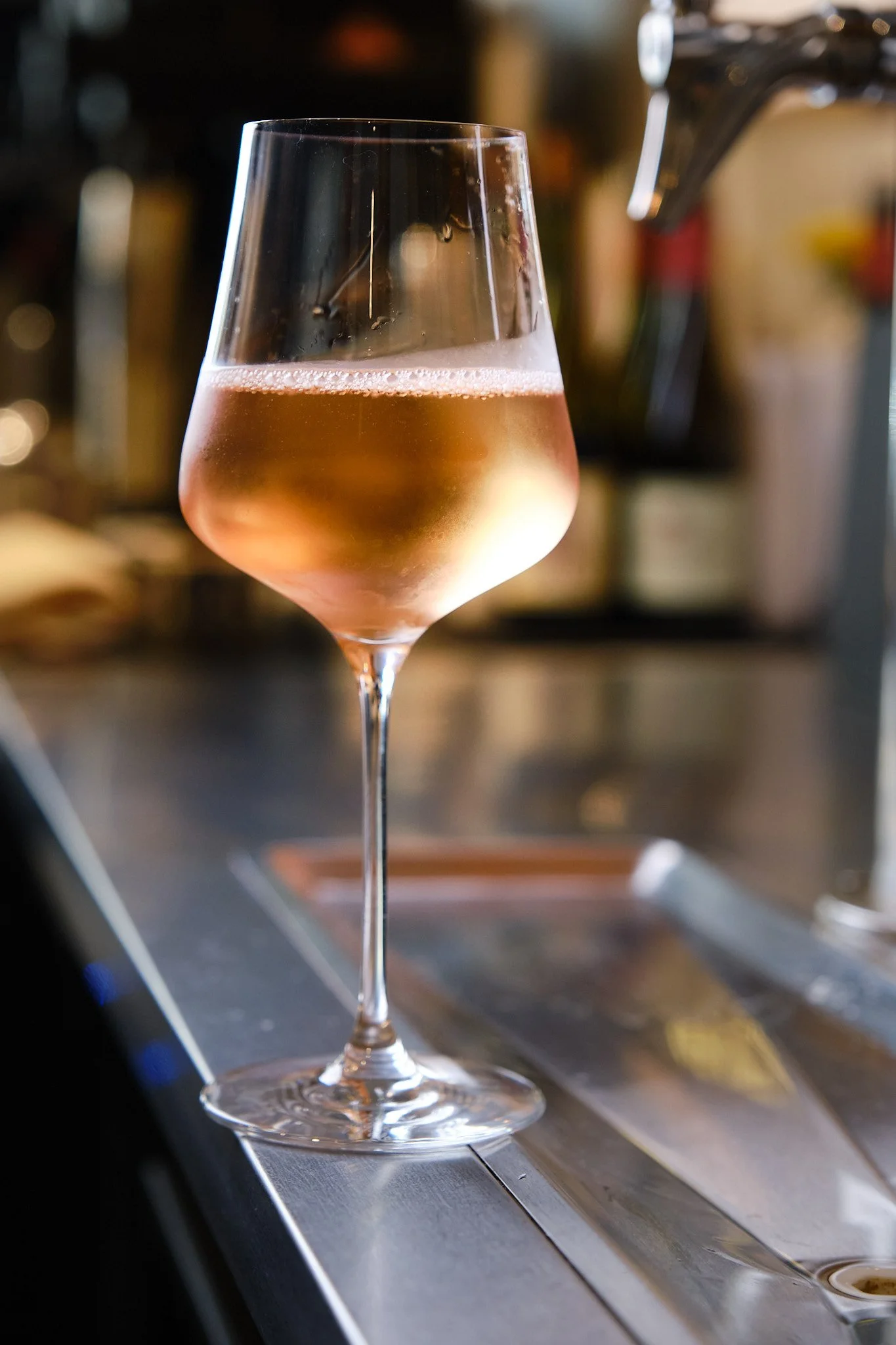A glass of rosé wine on a bar counter with a blurred background.