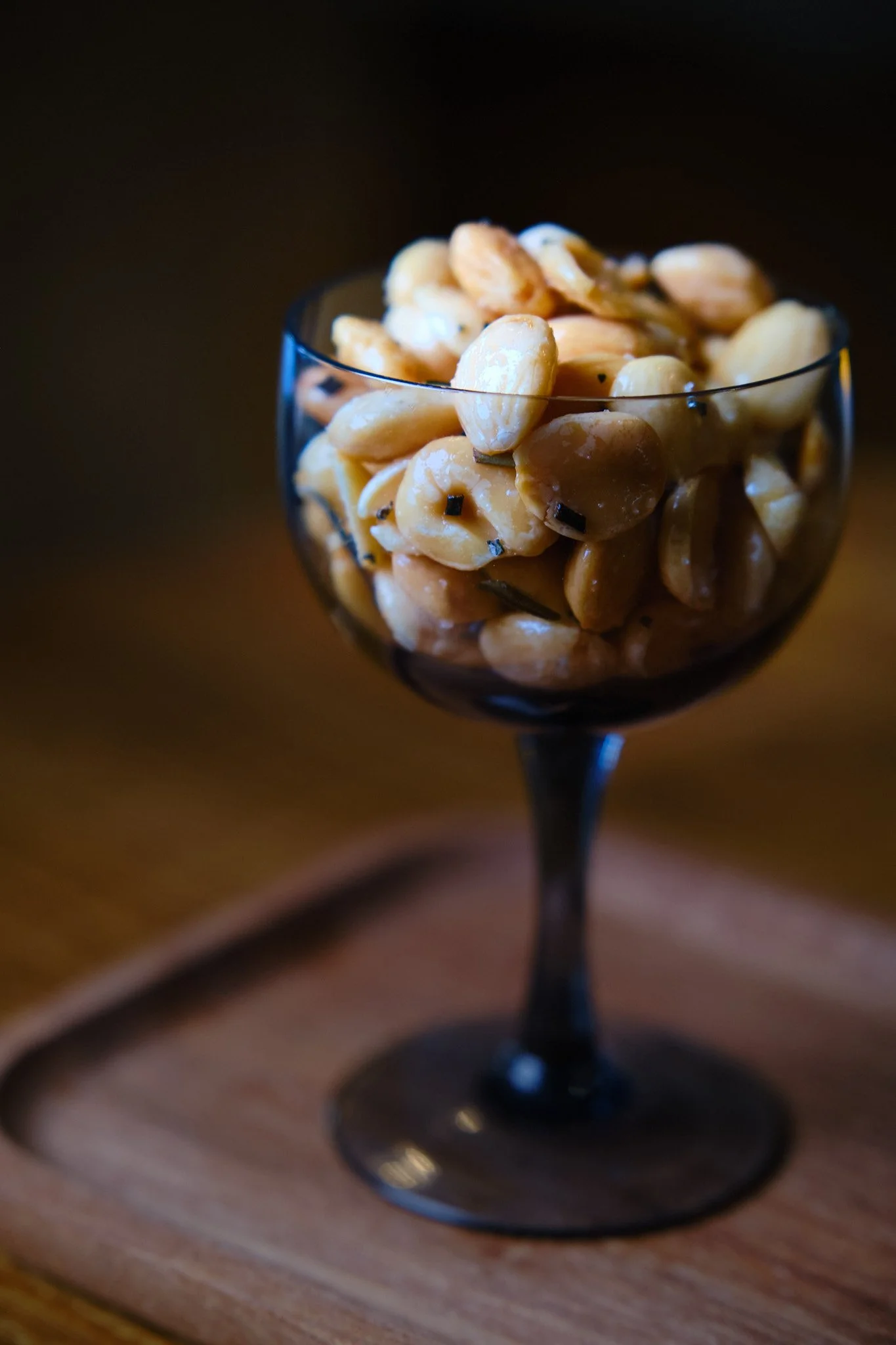 Close-up of a glass bowl filled with roasted cashew nuts on a wooden surface.