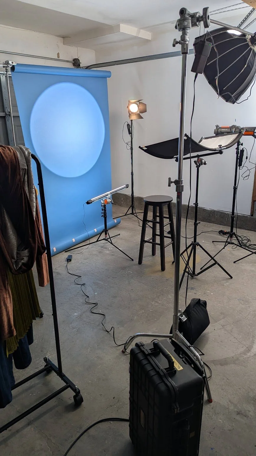 Photo of a photography studio setup with a blue backdrop, studio lights, a stool, and various equipment.