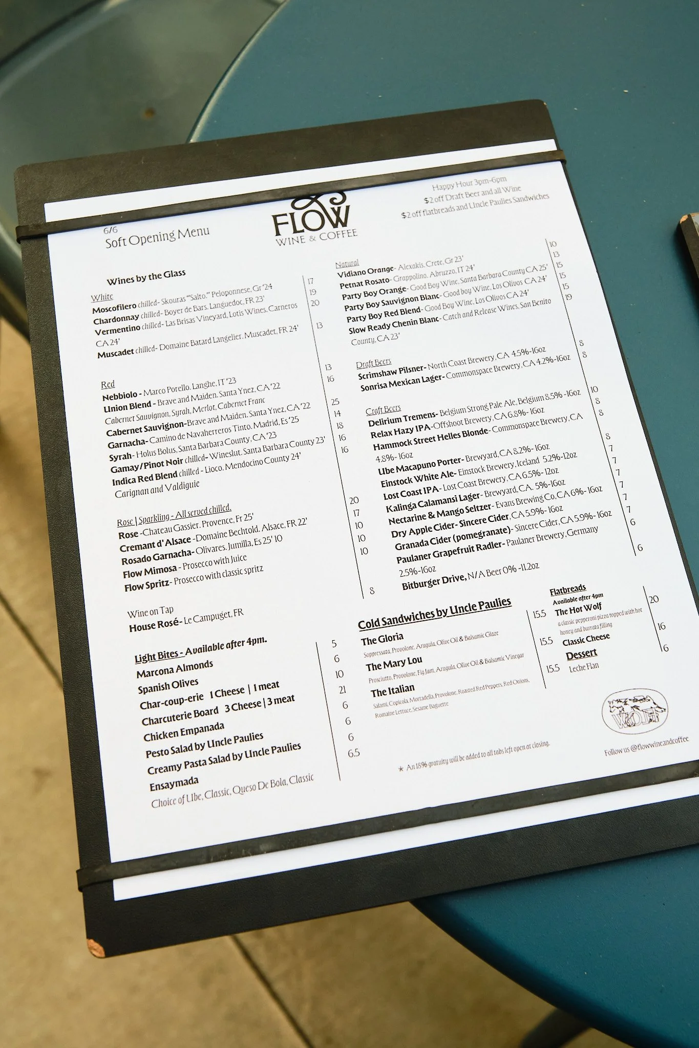 Menu from Flow Wine & Coffee restaurant featuring wine list and food options, placed on a black binder on a blue table.