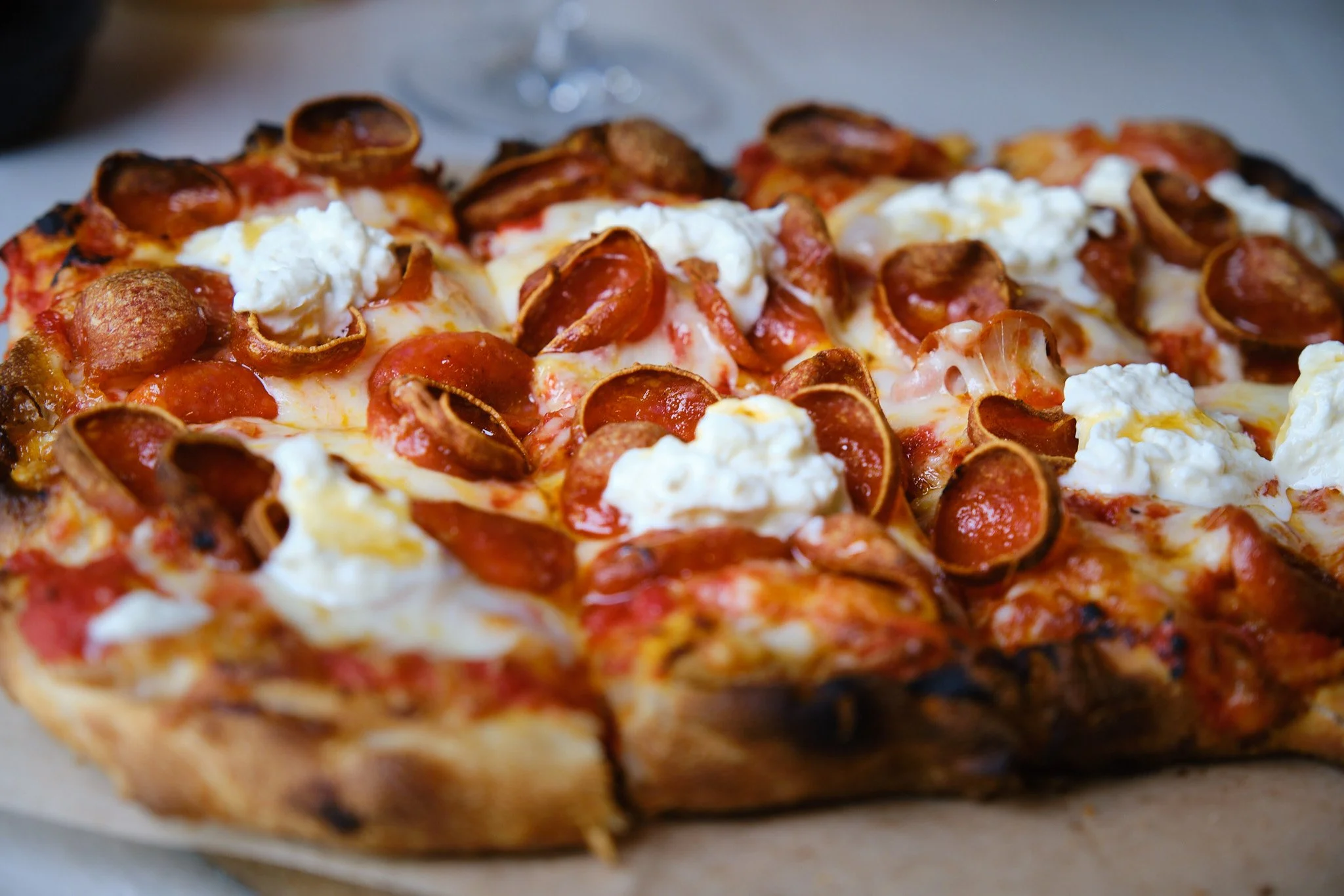 Close-up of a pepperoni pizza with melted cheese, dollops of ricotta cheese, and a crispy crust.