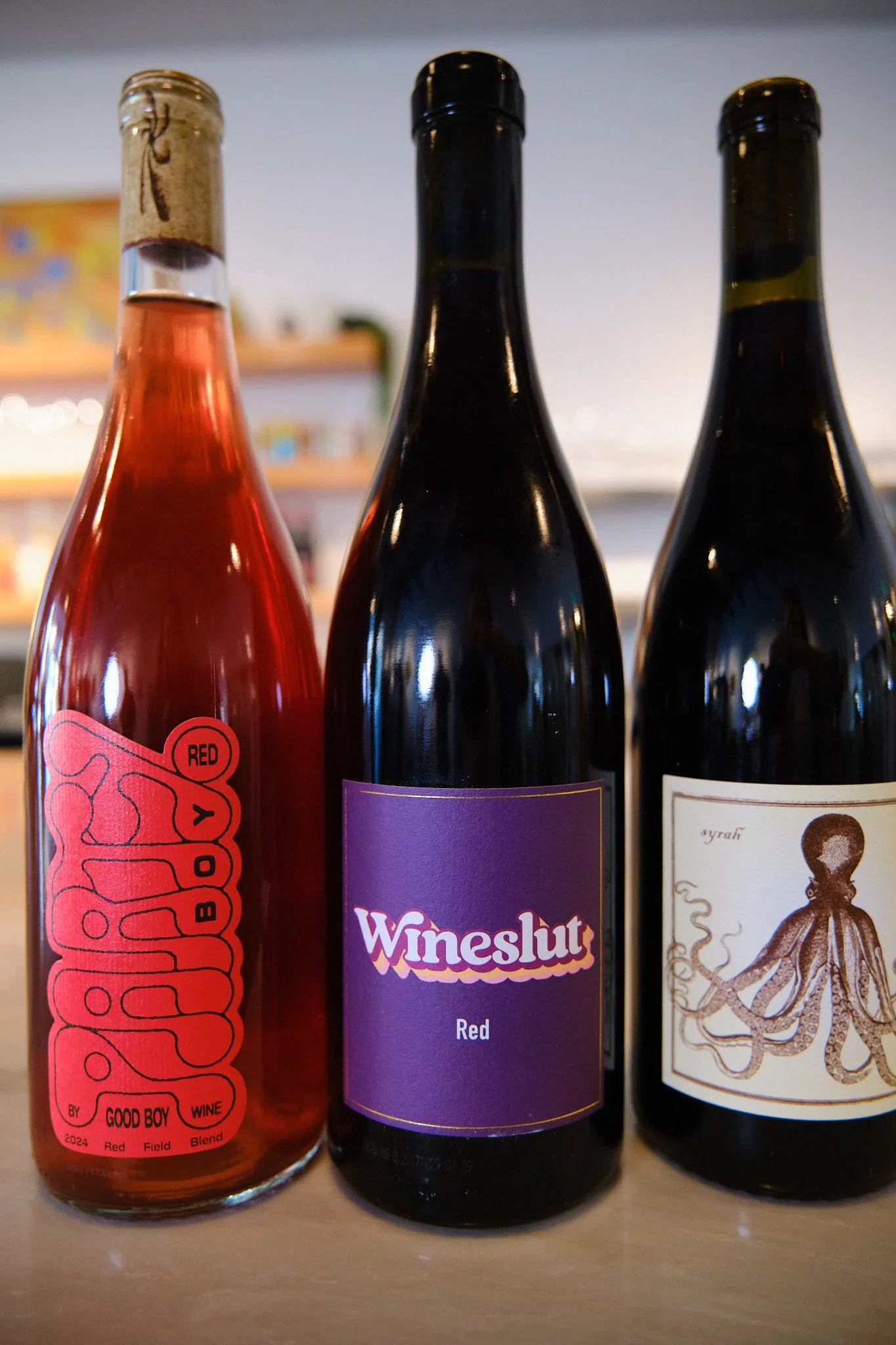 Close-up of three wine bottles on a wooden surface, with blurred background.