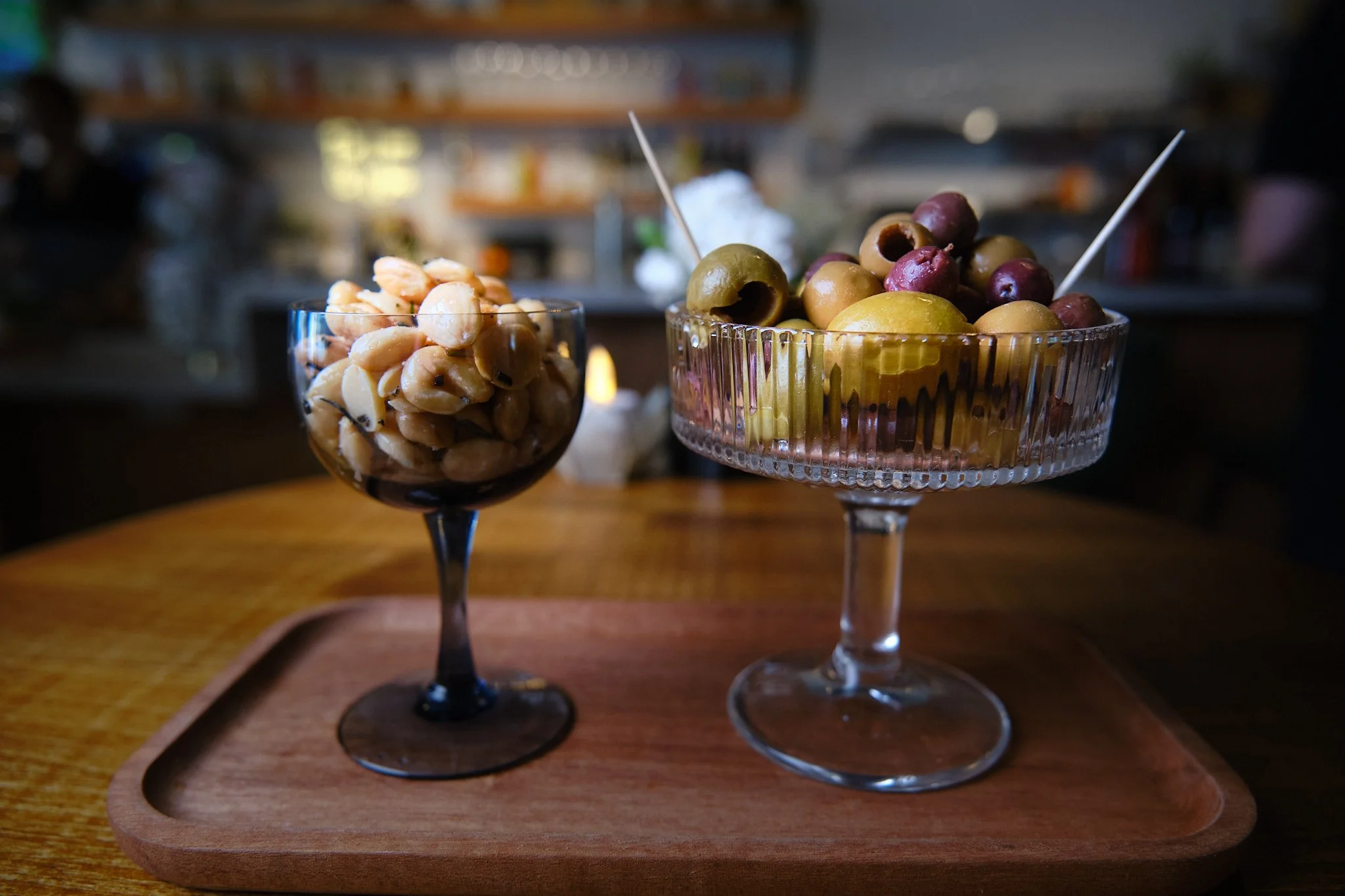 Two glass bowls filled with mixed olives on a wooden tray.