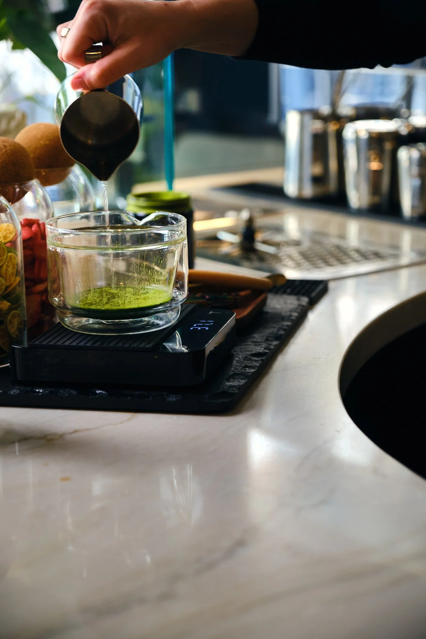 Person pouring black liquid into a glass on a black tray at a cafe or restaurant.