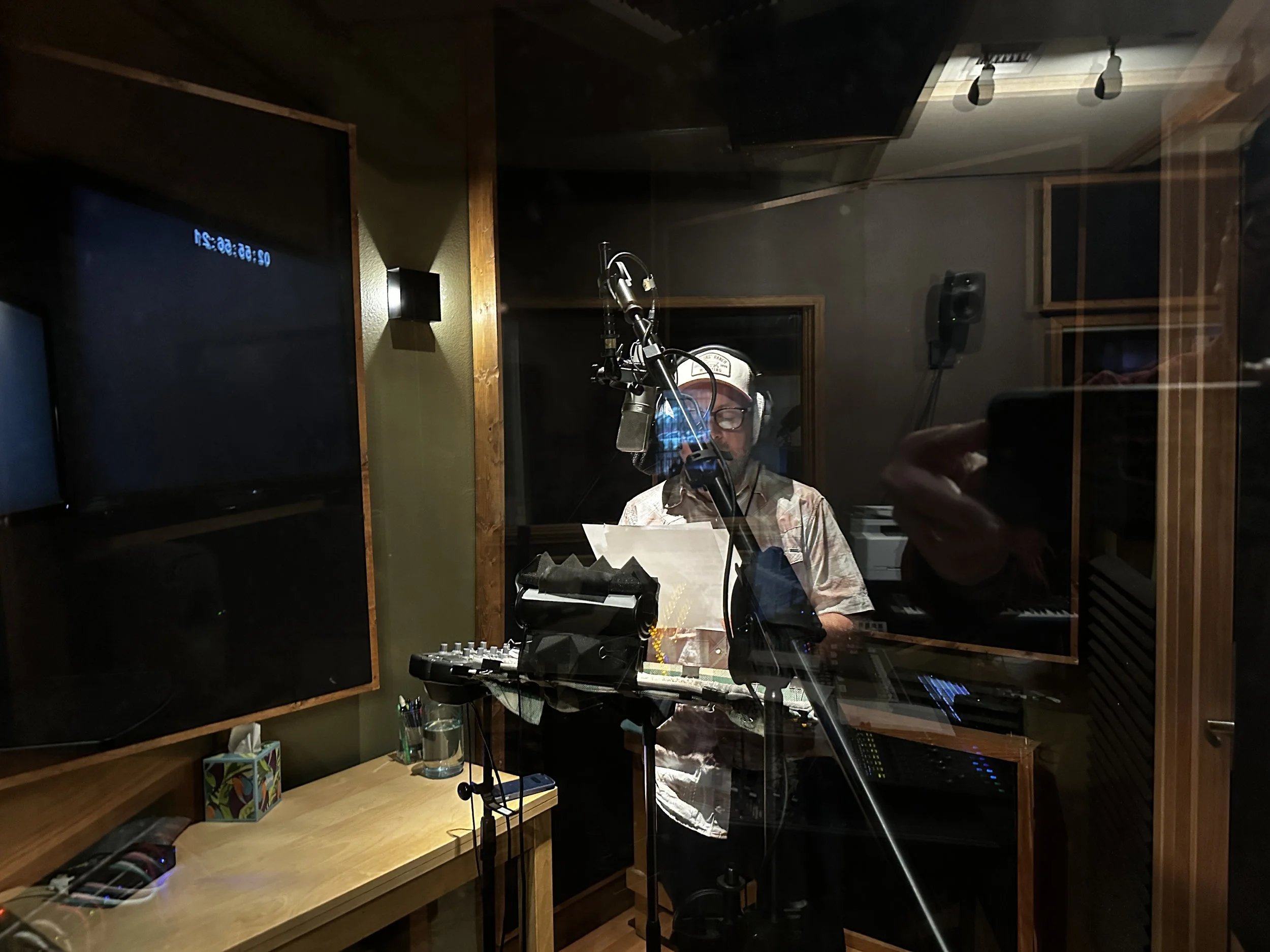 View through the window into the VO booth. The booth has it's own video monitor, and a separate ipad for zoom feeds.