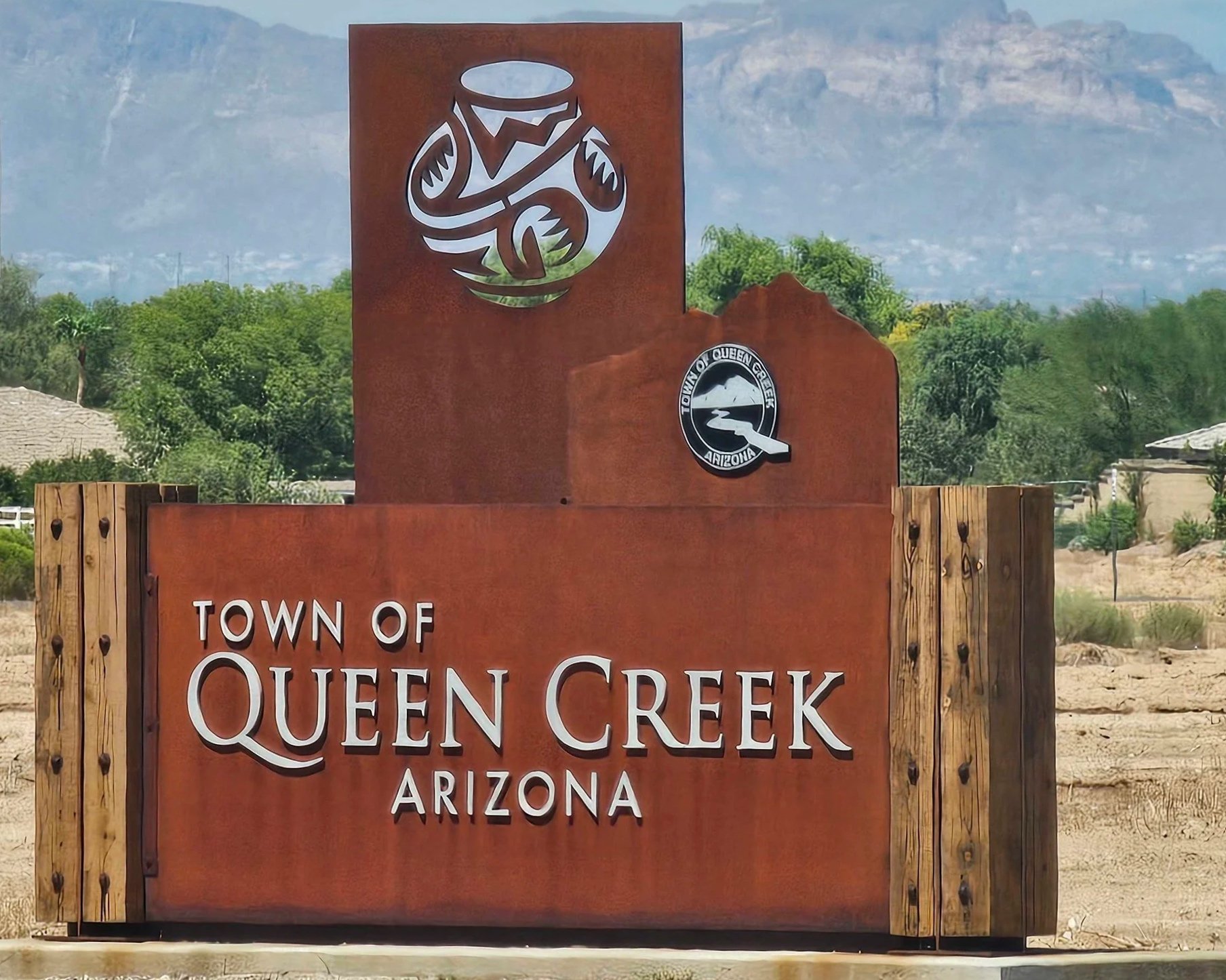 Wooden sign with cutout design of a guitar, mountain, and football, indicating the town of Queen Creek, Arizona.