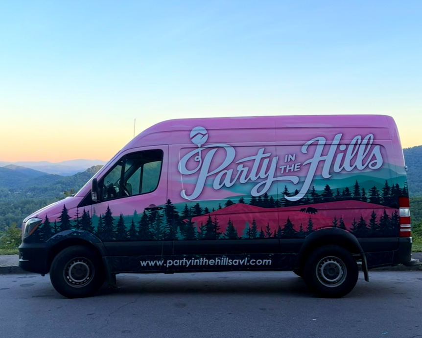 A pink van with a mountain landscape and forest design, and the text 'Party in the Hills' on the side, parked with mountains in the background during sunset or sunrise.