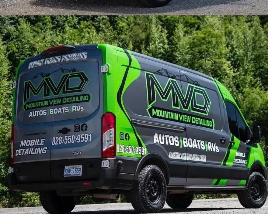 A black van with green and gray graphics advertising Mountain View Detailing, an auto, boat, and RV detailing service. The van displays a phone number and social media icons, with a mountain logo and the text 'MVD'.