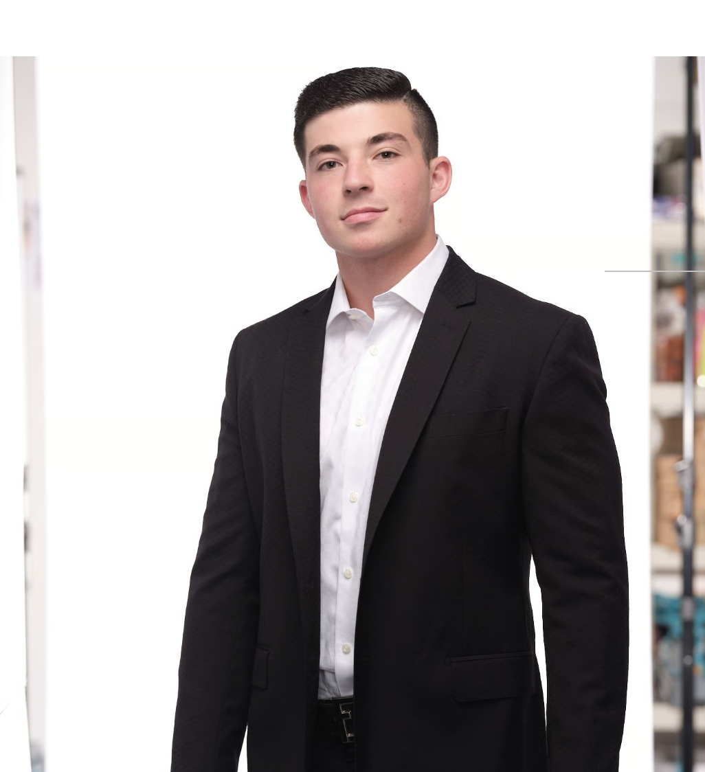 A young man in a black suit and white dress shirt posing against a plain white background.