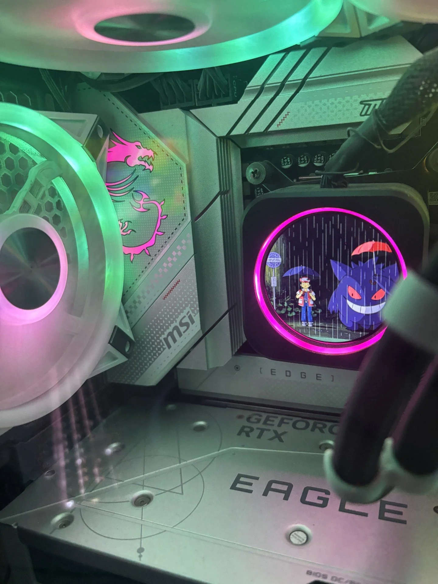 Close-up of a gaming computer interior with RGB lighting, featuring a Dragonite and Gengar Pokémon on a display screen.