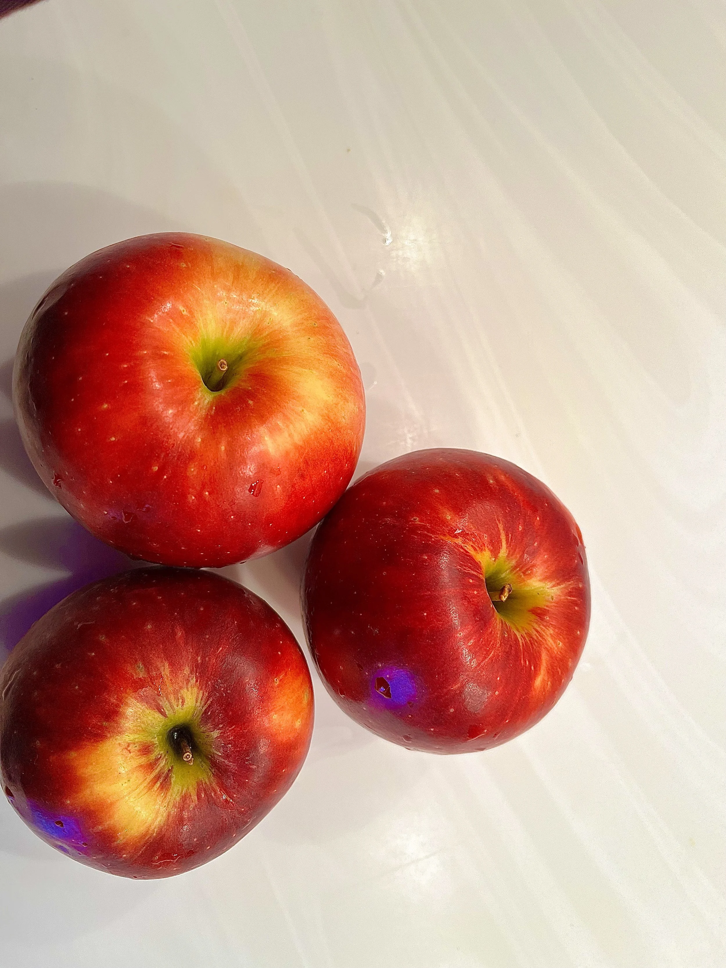 Three red and yellow apples resting on a white surface.