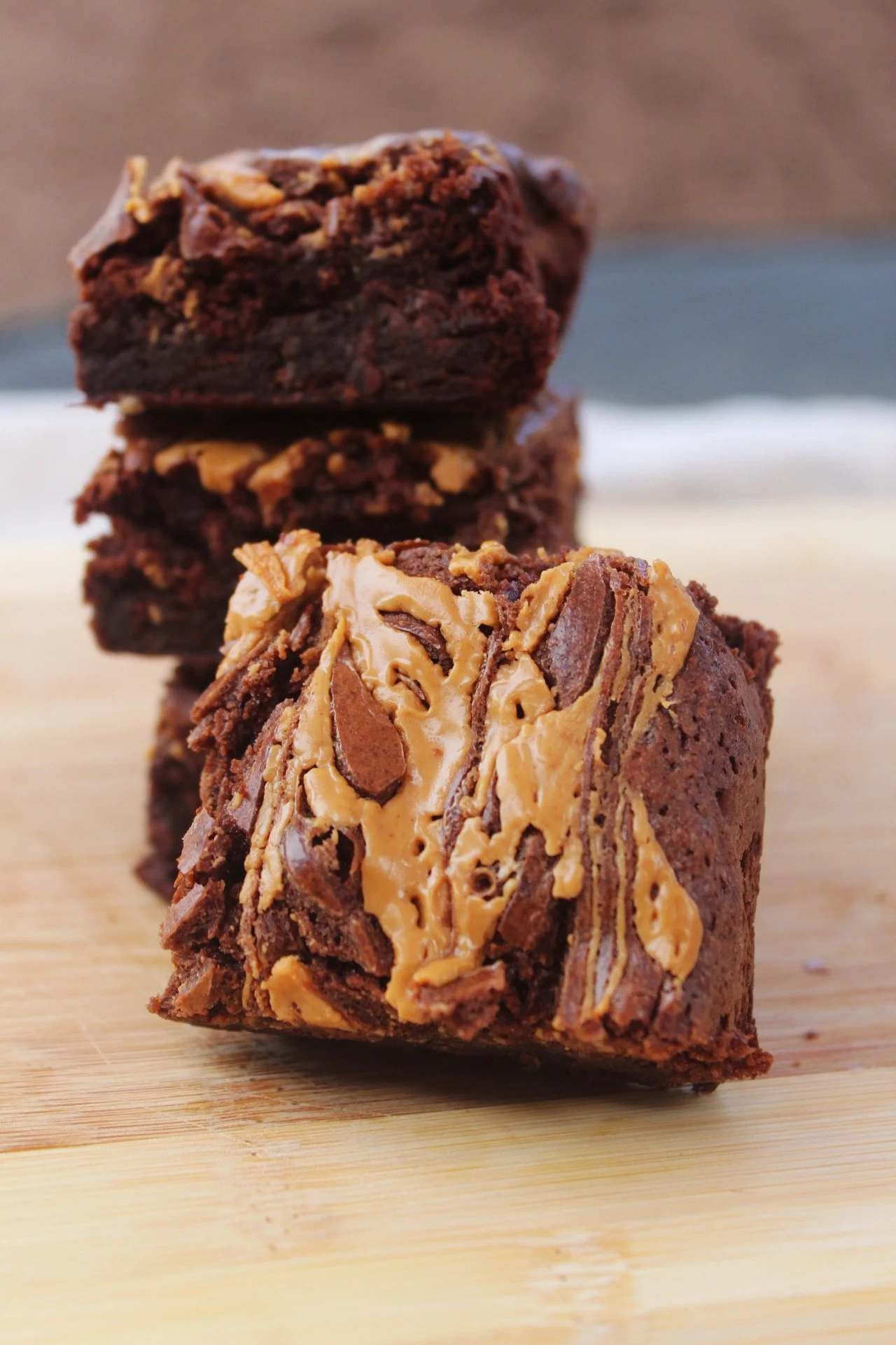 Close-up of three chocolate and peanut butter chunk brownies stacked on a wooden surface.