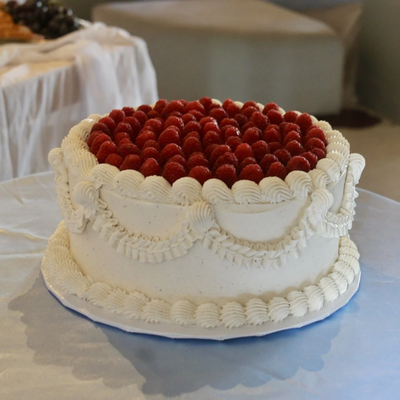 A round white frosted cake decorated with whipped cream and topped with fresh raspberries.