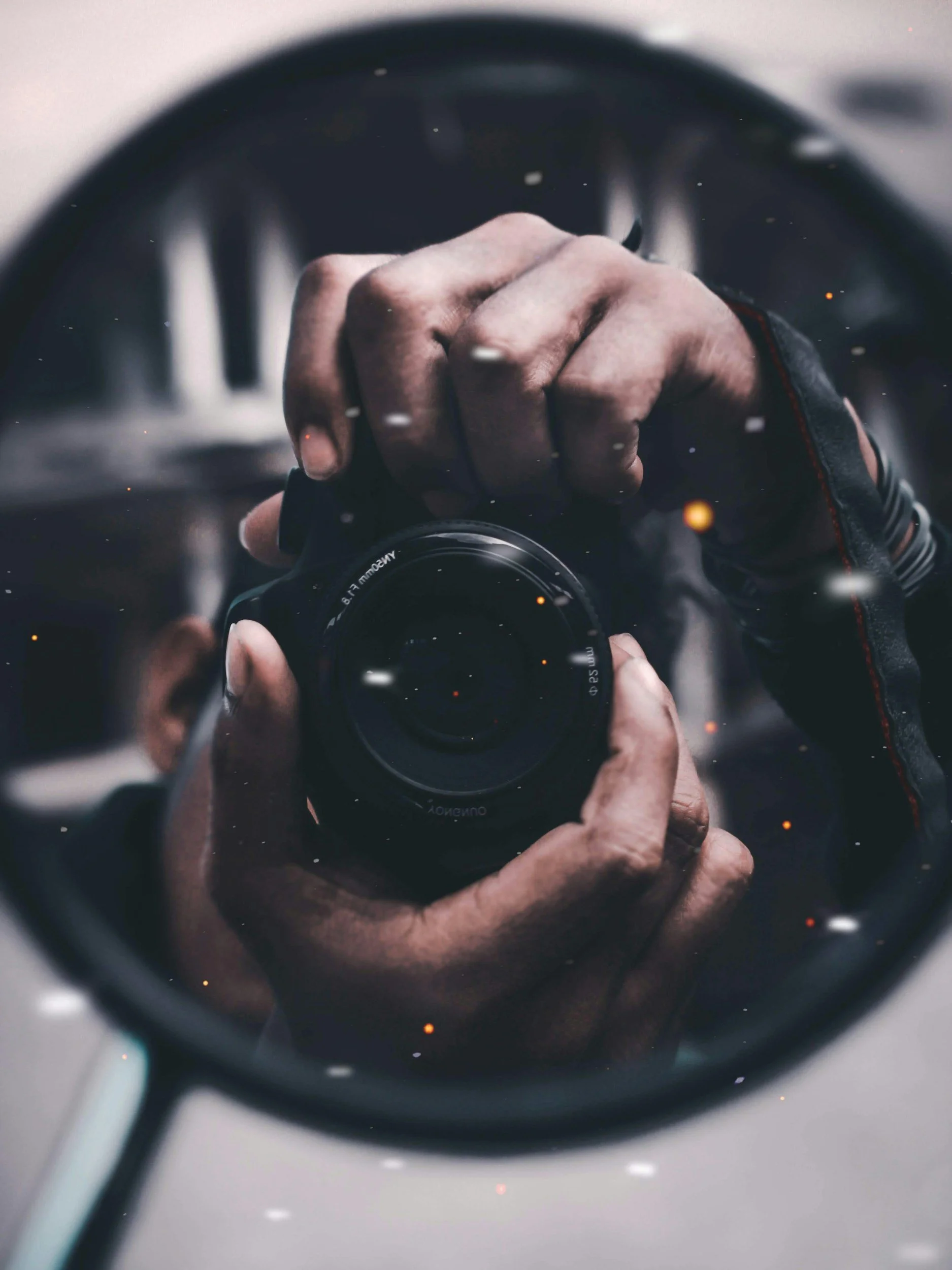 A person taking a photo of themselves using a camera, reflected in a shiny surface. The hand is wearing a black glove with red accents.