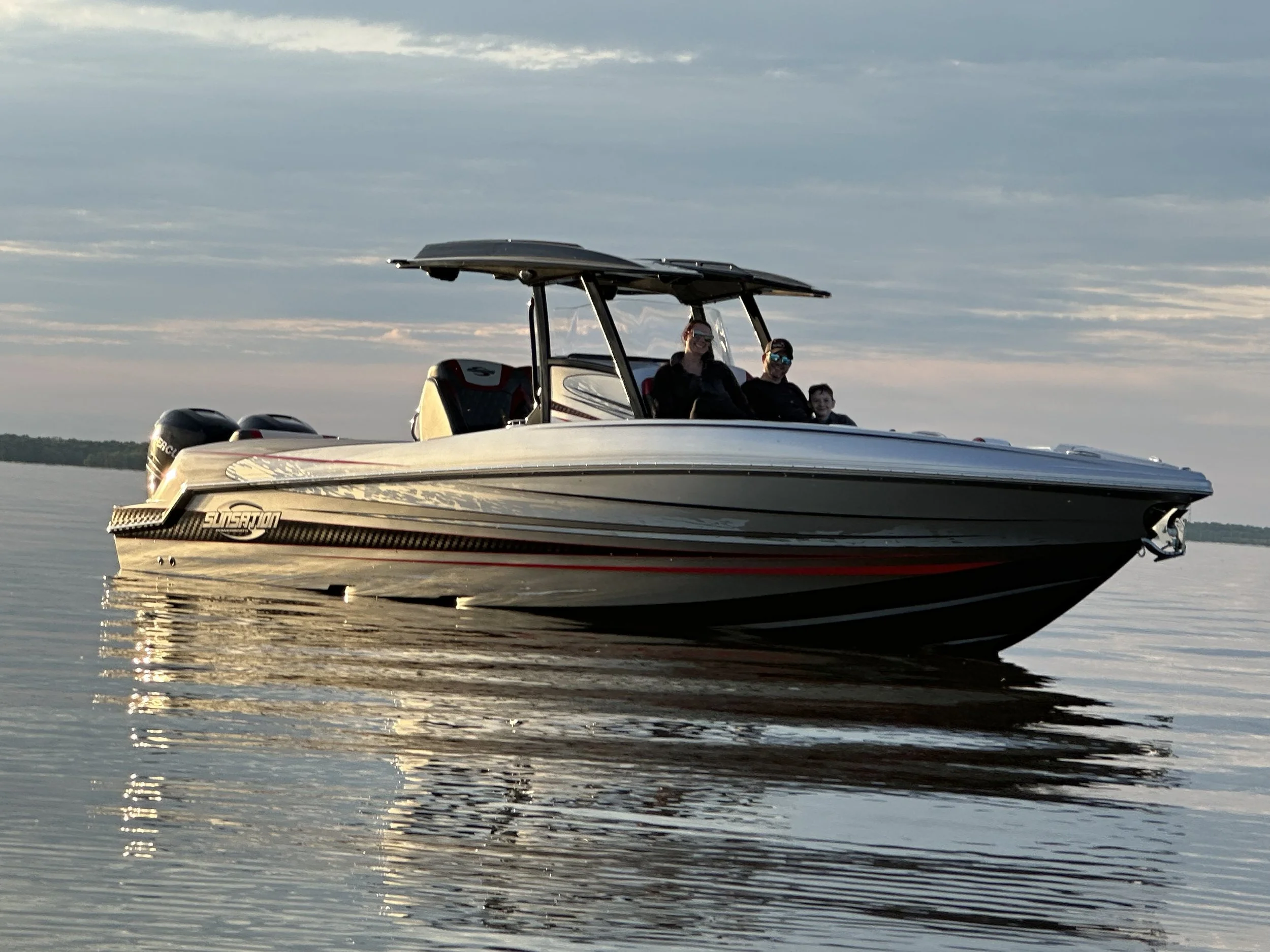 A boat with three people on board sailing on a lake during sunset.
