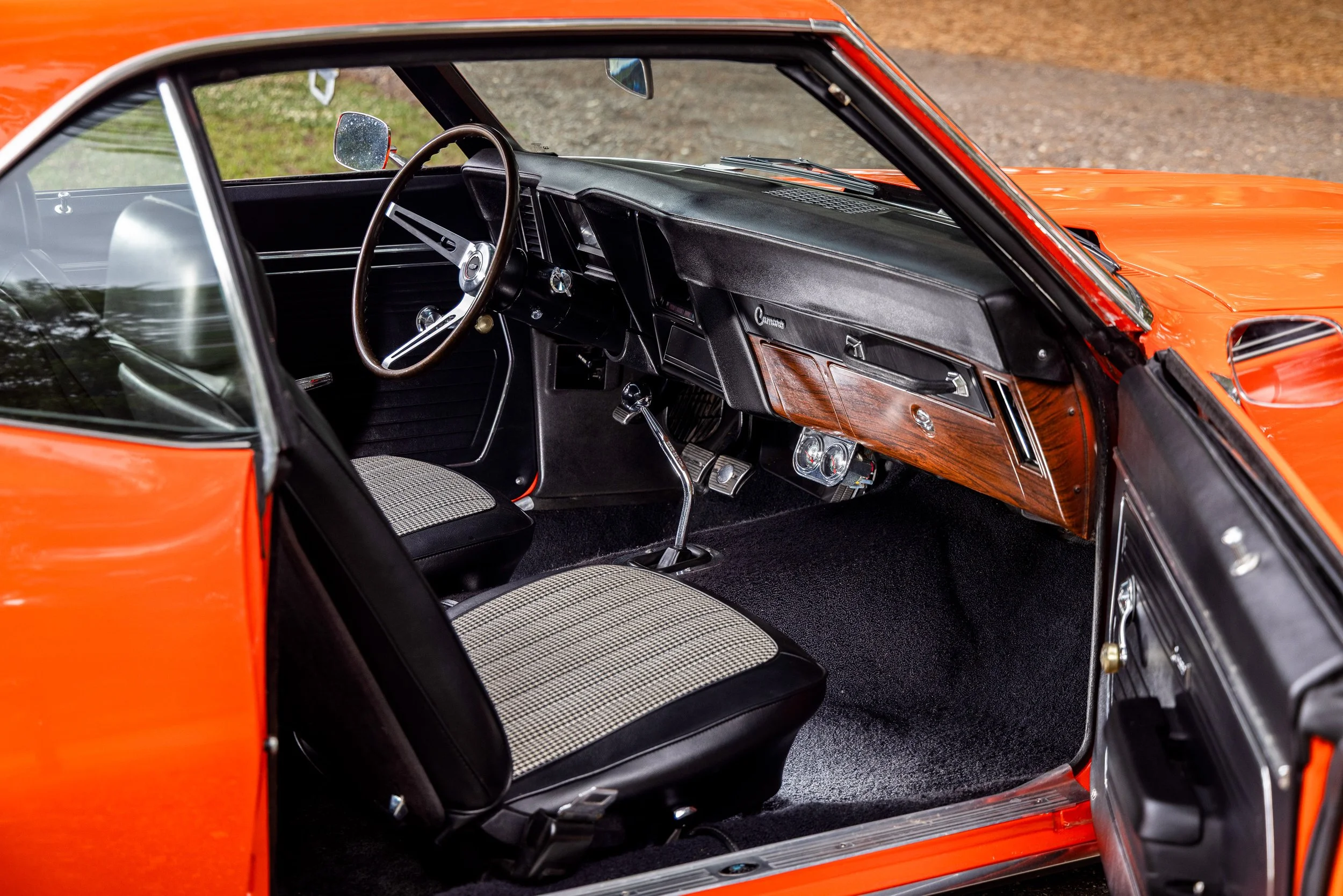 Interior of a vintage orange car showing steering wheel, dashboard, front seats, and gear shift.