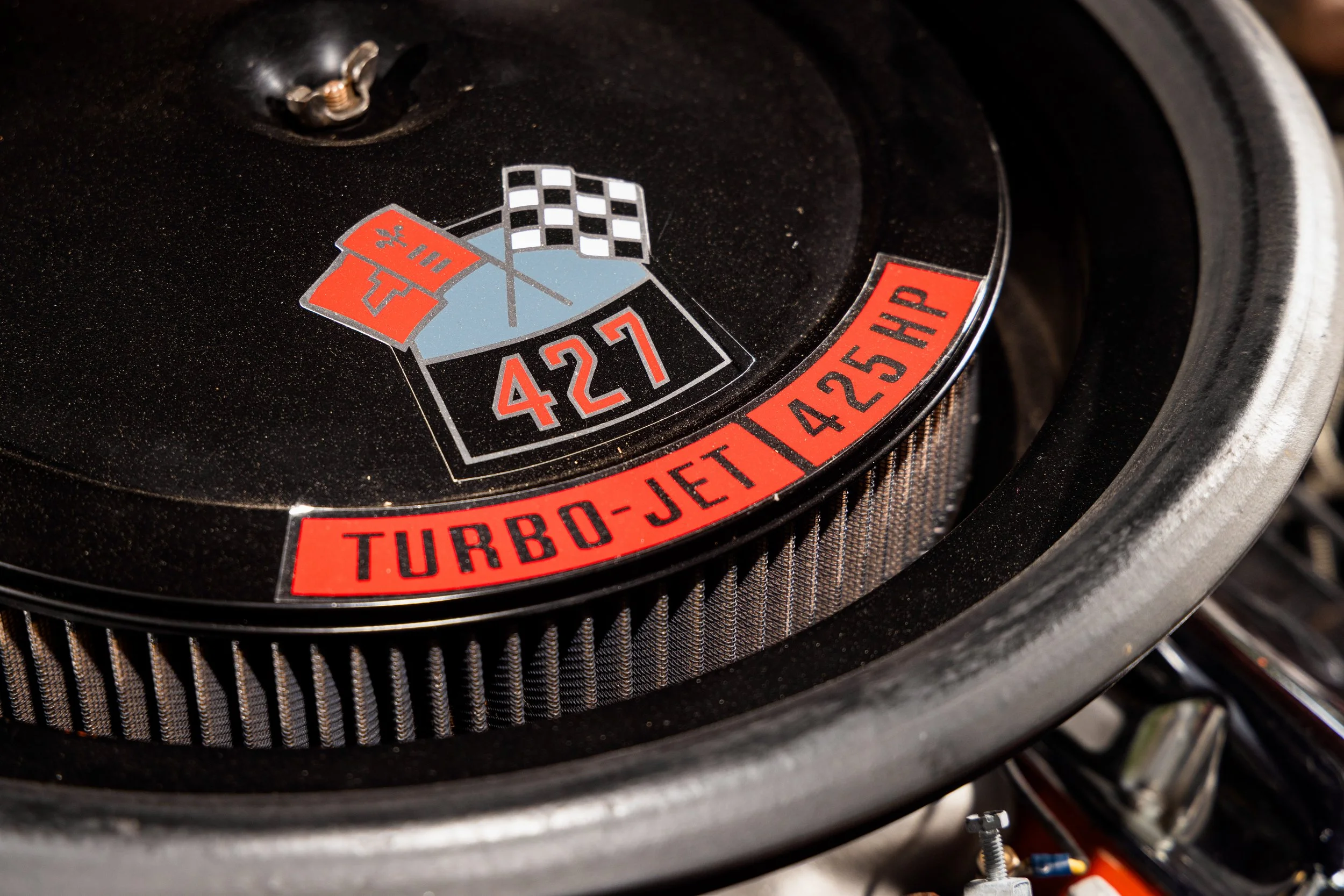 Close-up of a racing car engine component with a logo that includes a checkered flag, a red flag, the number 427, and a red banner that says "TURBO-JET 425 HP."
