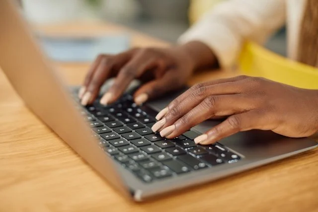 Close-up of person typing on a laptop keyboard at a wooden desk.