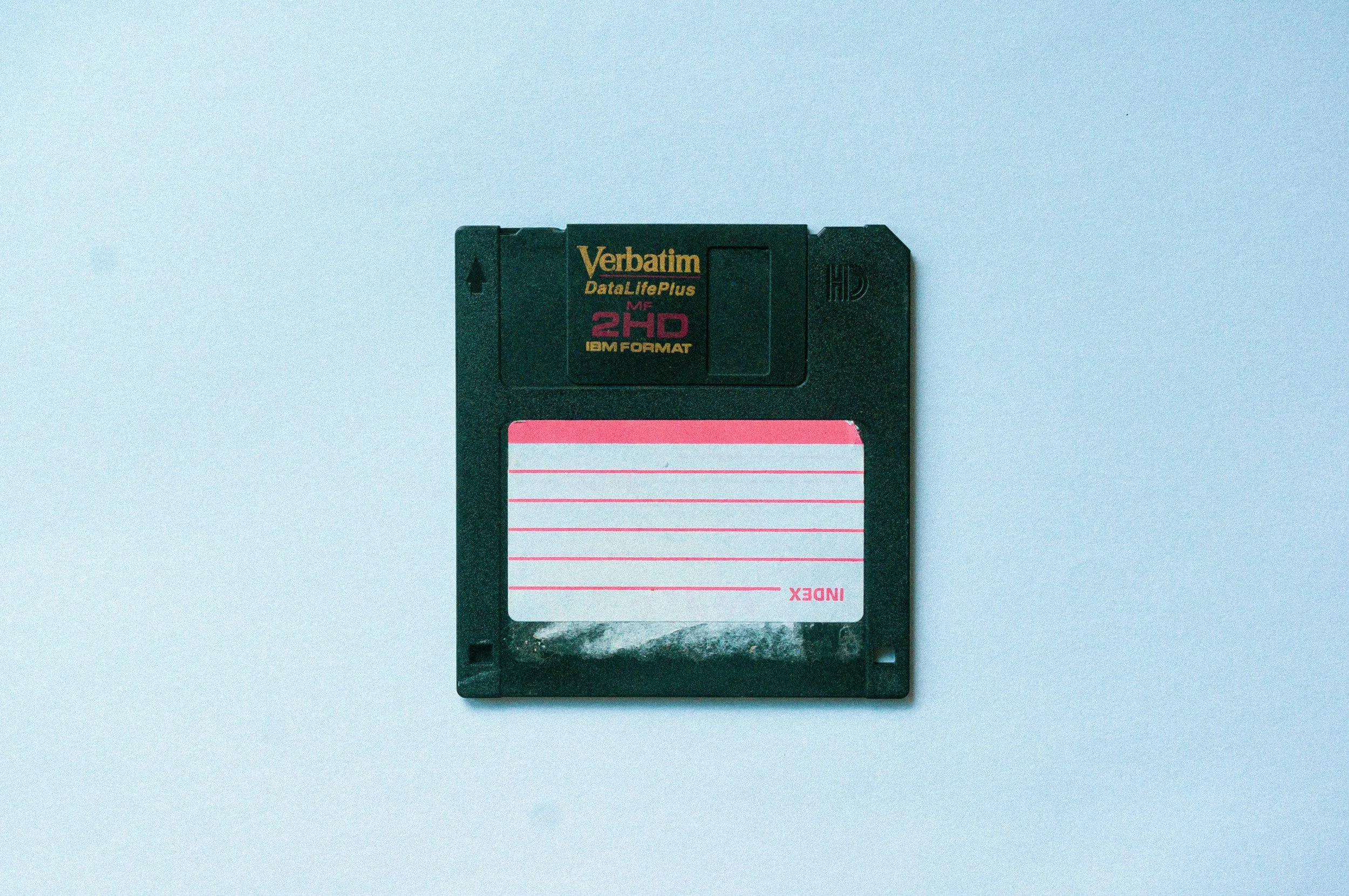 A vintage Verbatim DataLifePlus 2HD floppy disk with a black plastic shell and a pink and white label on a light blue background.