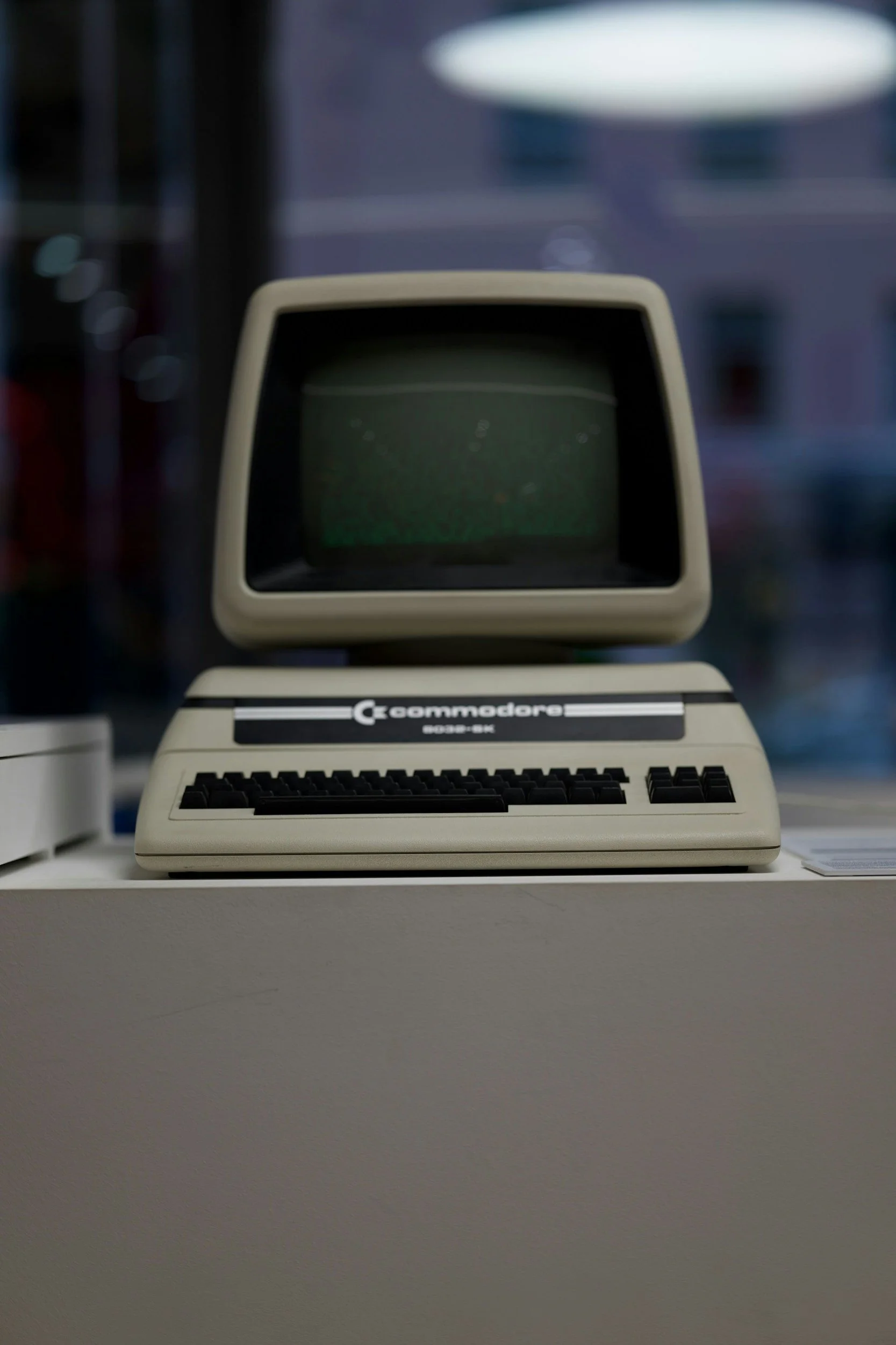 Close-up of an old vintage Apple Macintosh computer with a black screen and a beige keyboard, placed on a white surface, with a blurred background.