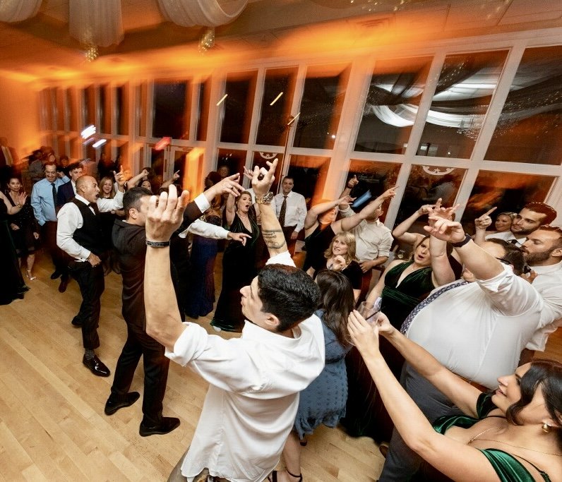 People dancing and enjoying a celebration or party in a large, brightly lit room with wooden floors and large windows.