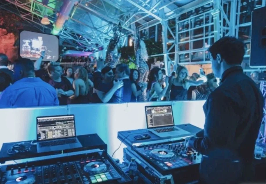 DJ performing at a nightclub with a crowd dancing and socializing in the background.