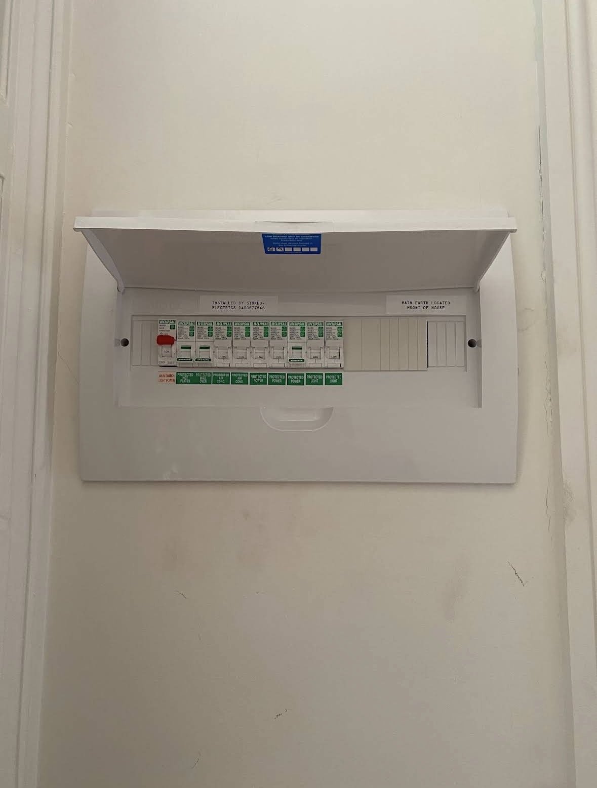 Electrical breaker panel with open cover, mounted on a white wall.