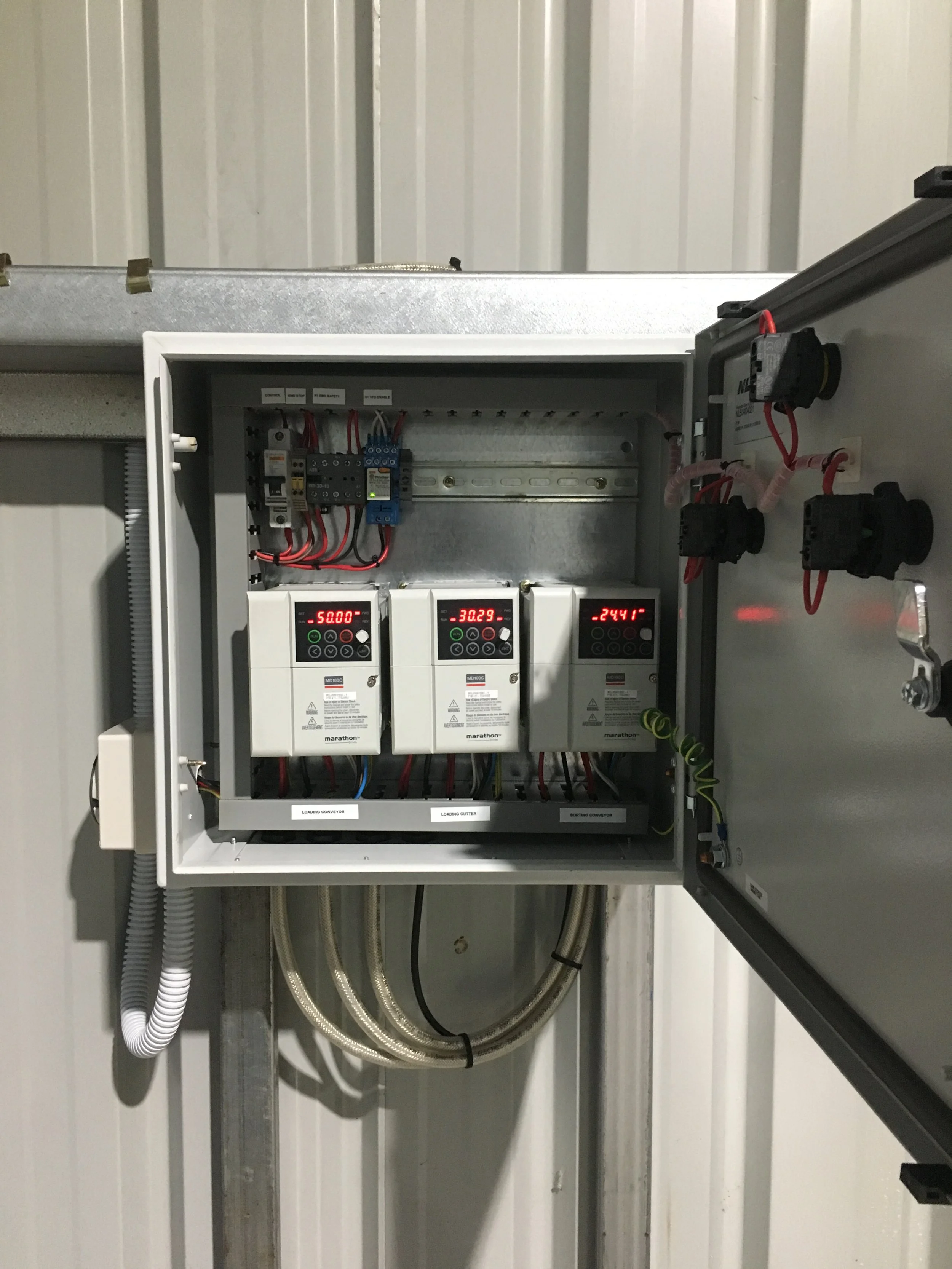 Electrical control panel with digital displays, wiring, and components installed in a metal box on a wall.