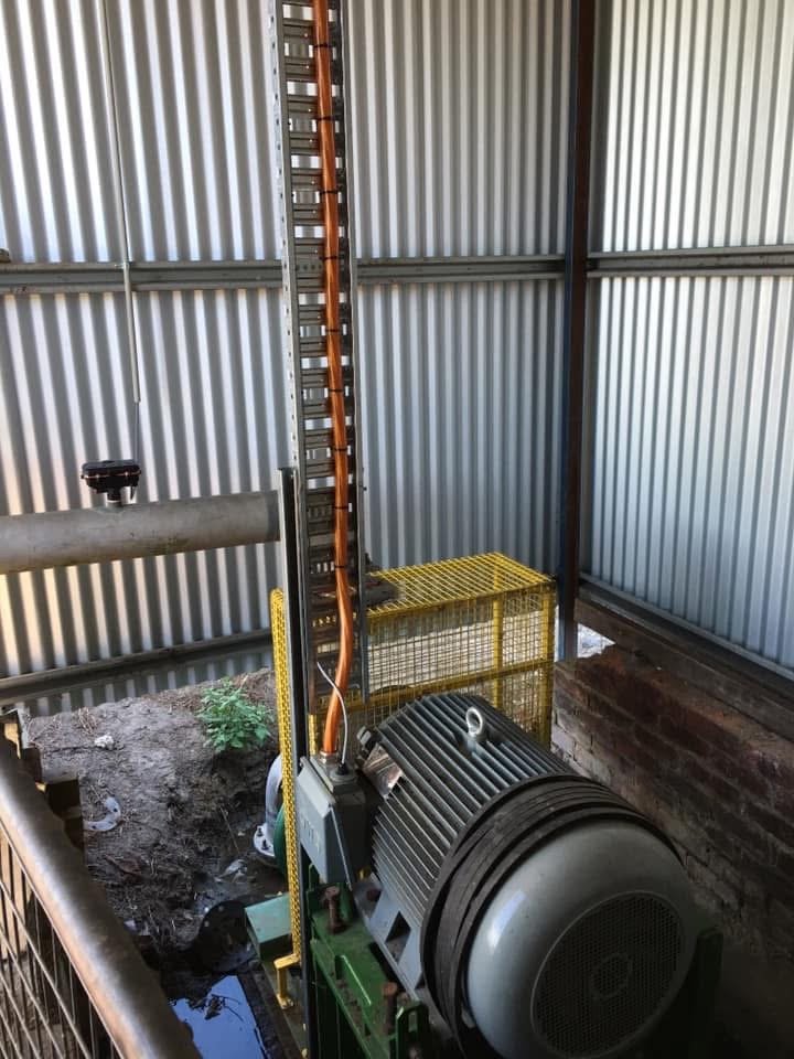 Industrial machinery with a large electric motor, pipes, and metal framing inside a shed with corrugated metal walls.
