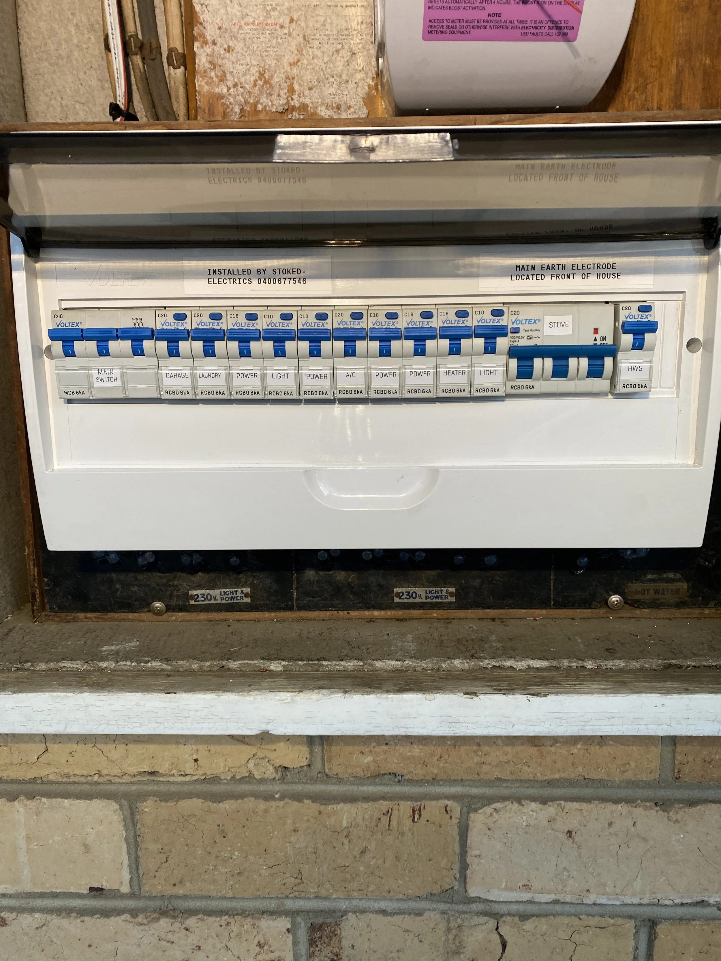 Electrical breaker box with labeled switches and circuit breakers mounted on a brick wall.