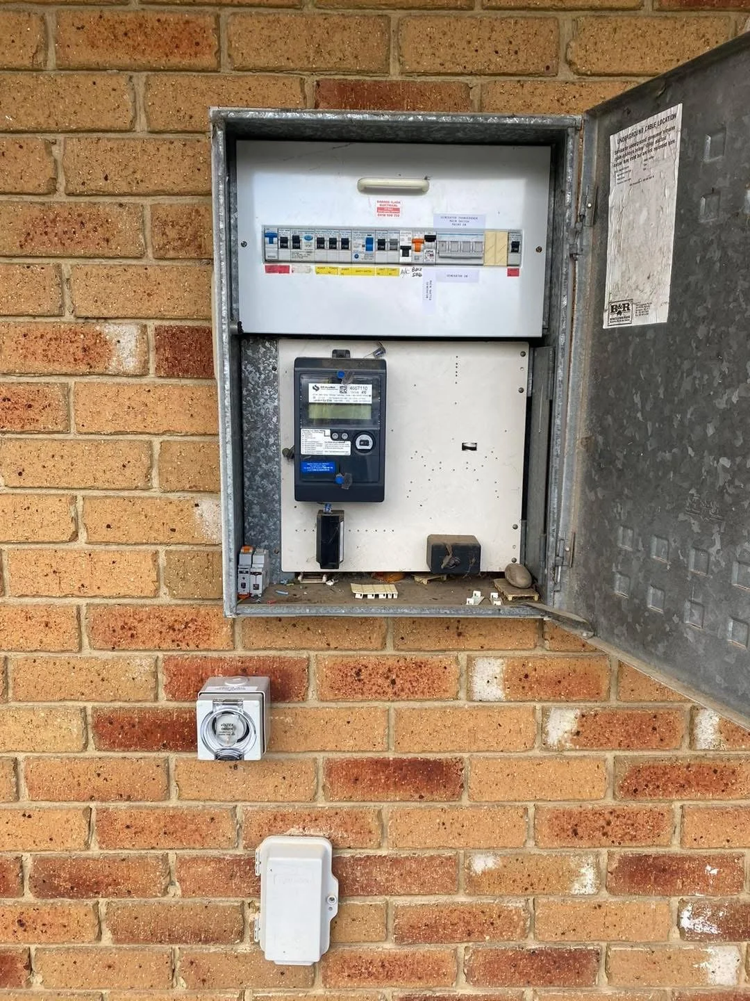 Electrical meter and circuit breaker box mounted on a brick wall.