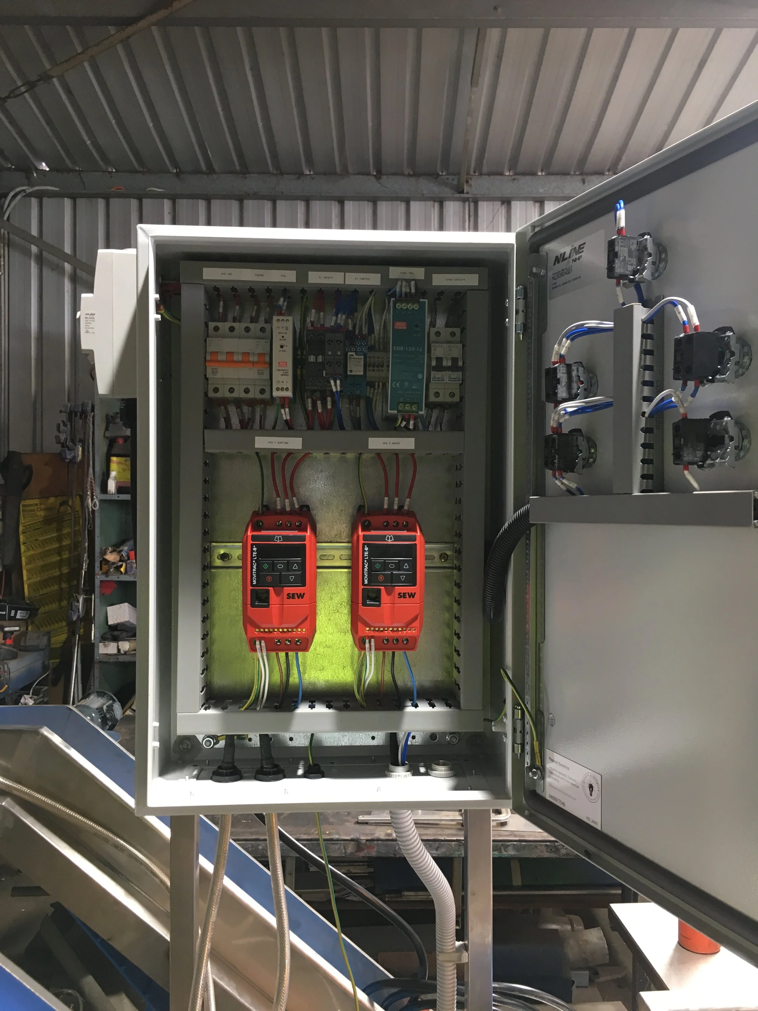 Open electrical control panel with wiring and components inside, and two red handheld devices hung on hooks at the bottom.