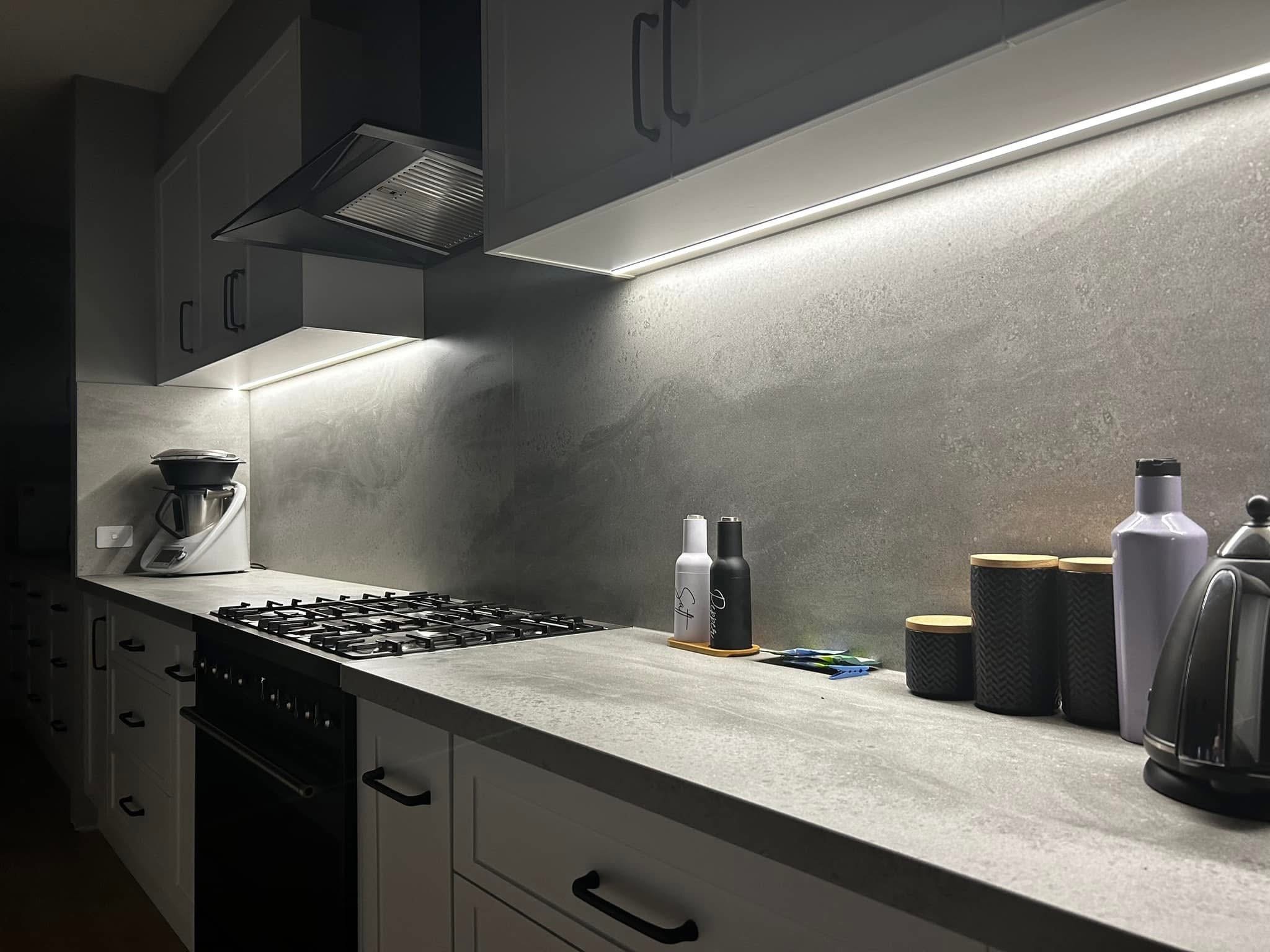 Modern kitchen countertop with kettles, bottles, and kitchen utensils, under cabinets with built-in lighting.