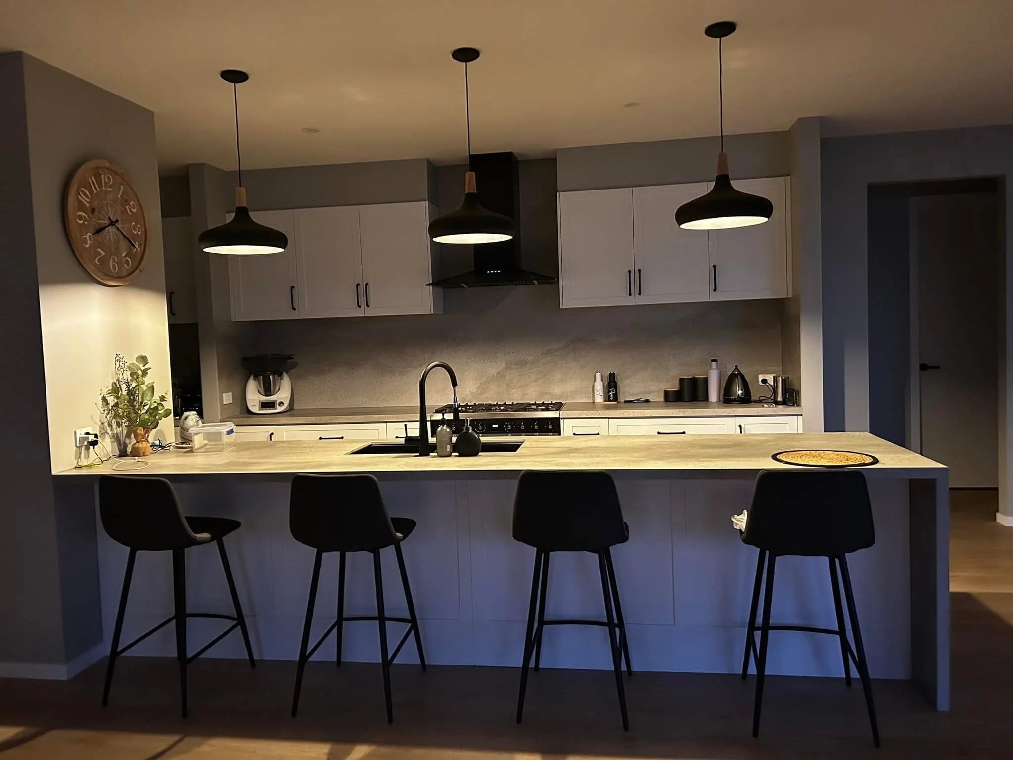 Modern kitchen with white cabinets, black pendant lights, and barstools at a kitchen island.