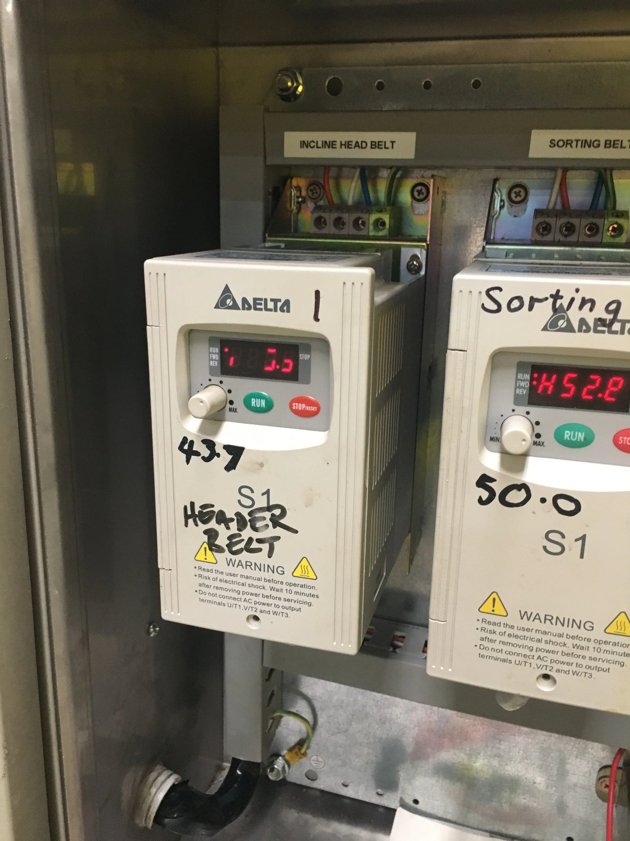 Close-up of electrical components within a metal enclosure, including a white device labeled 'Delta' with digital display showing '1.3', and written notes including '437' and 'HEADER BELT', suggesting a control or power system.