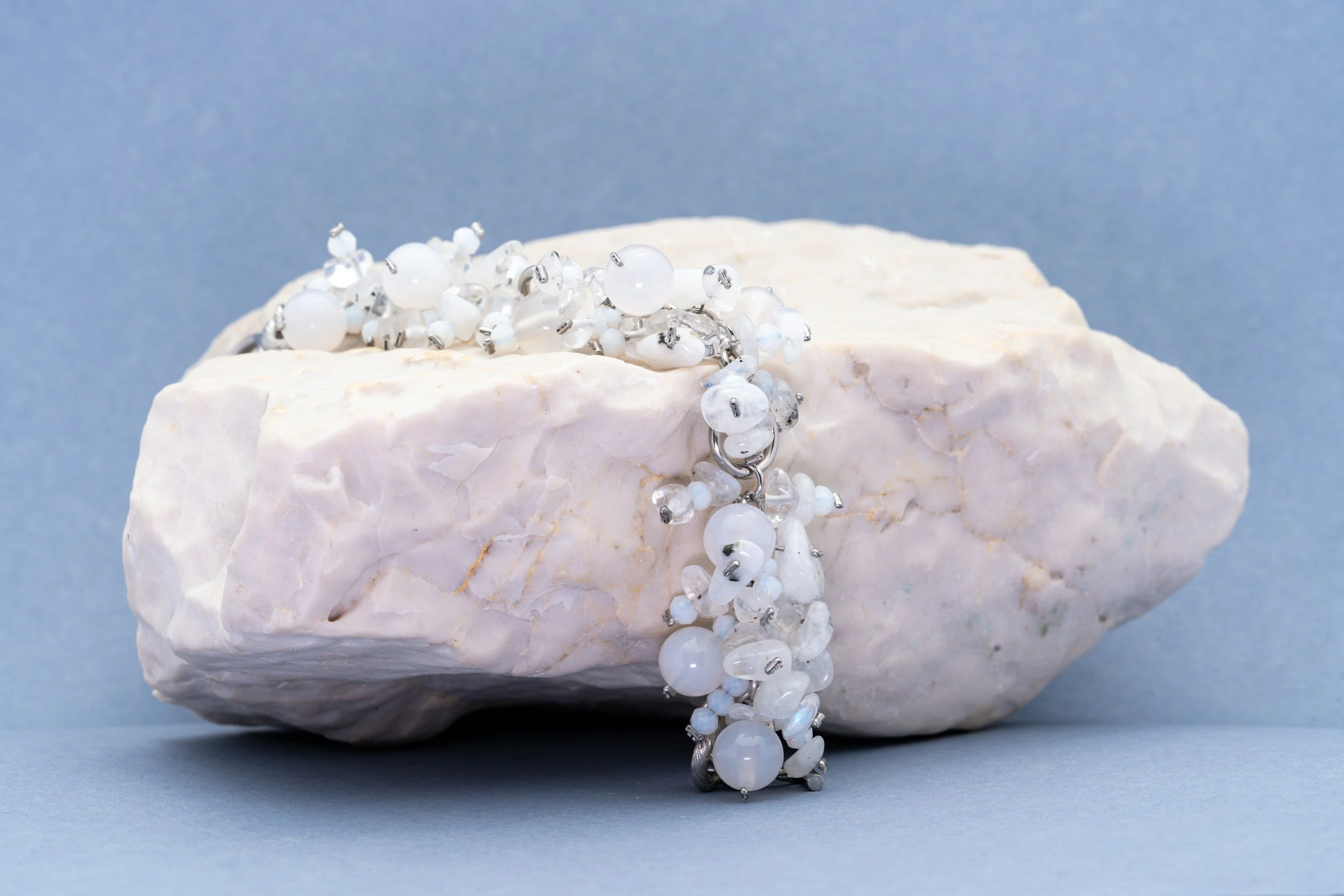 A white rock with a tangled white and clear beaded necklace draped over it, set against a blue background.