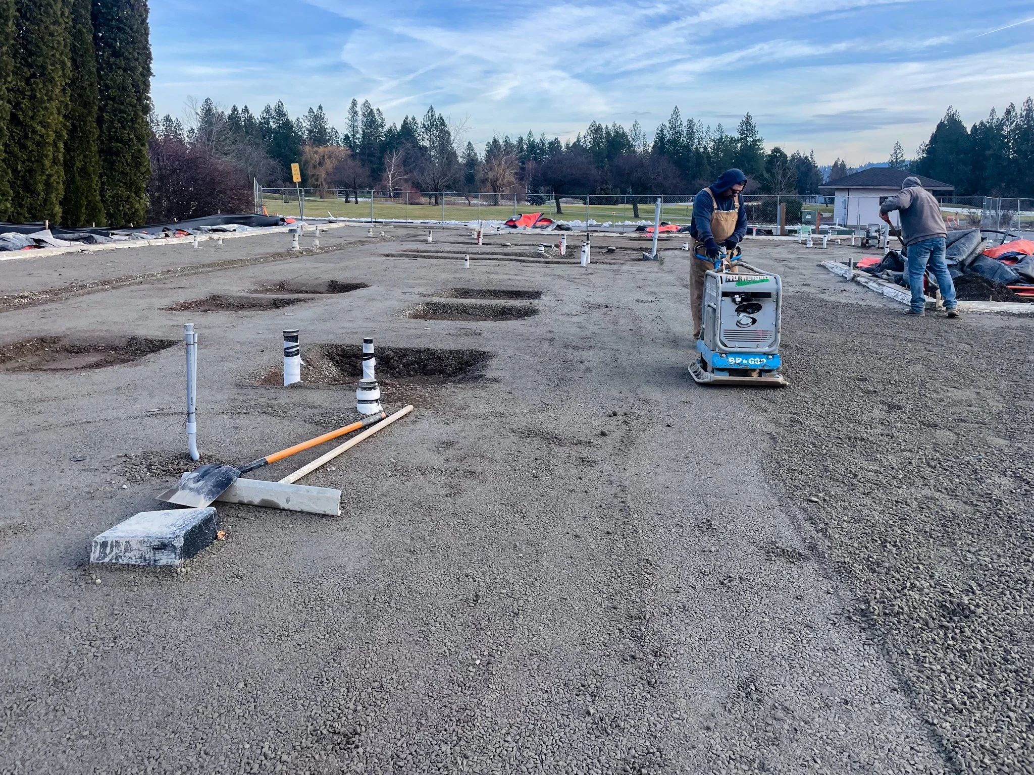 Construction workers installing a foundation at a construction site on a clear day, with holes in the ground for future concrete pillars.