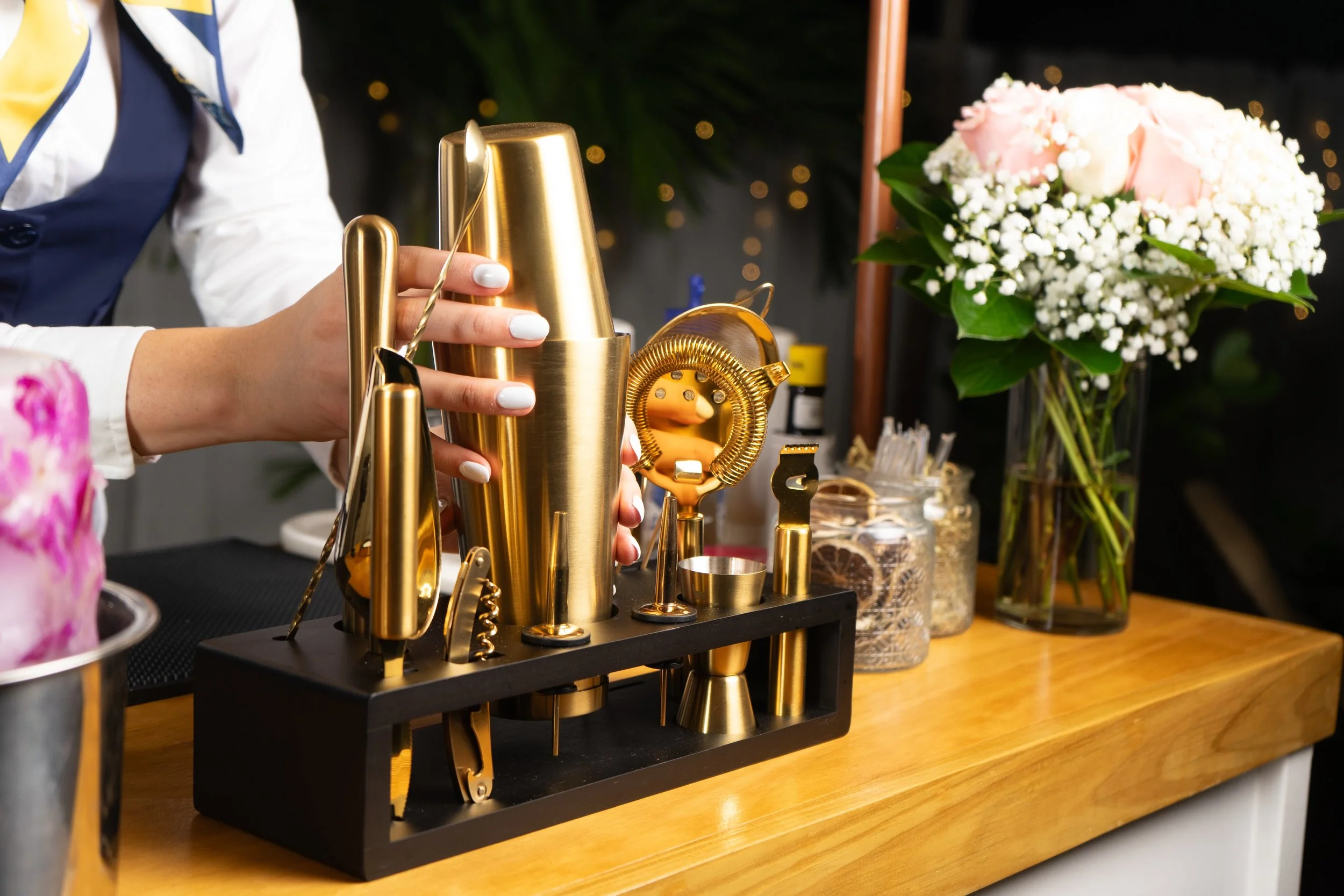 A bar setup with gold bar tools and a flower bouquet in the background.