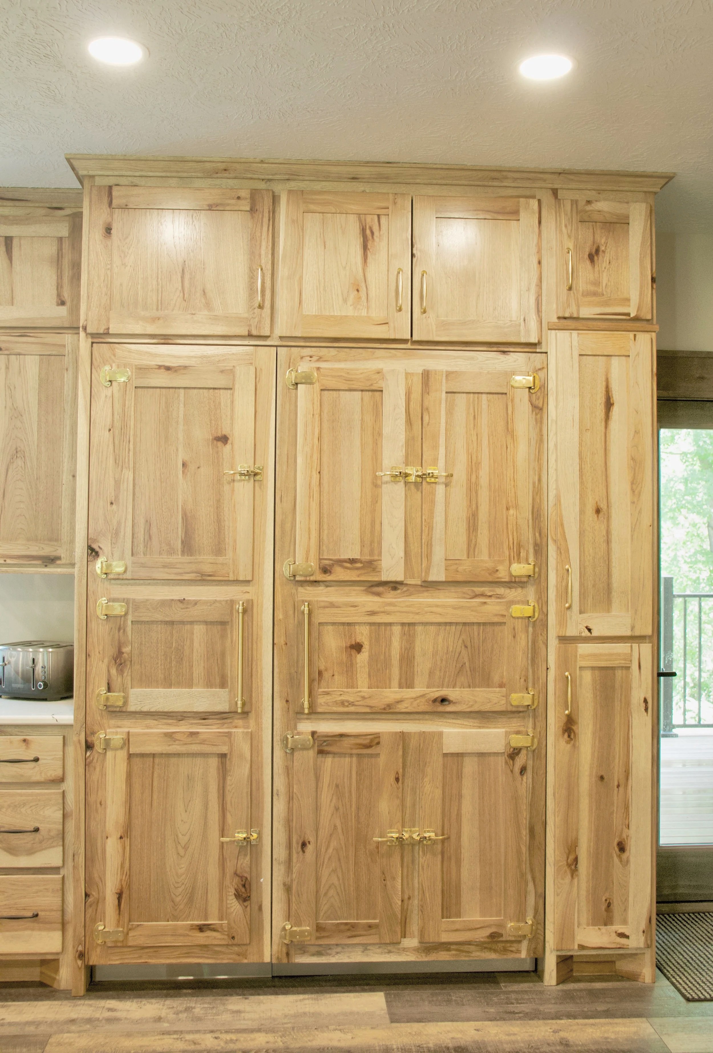 Wooden kitchen cabinets with gold handles in a bright room. Part of a countertop with a toaster visible on the left.