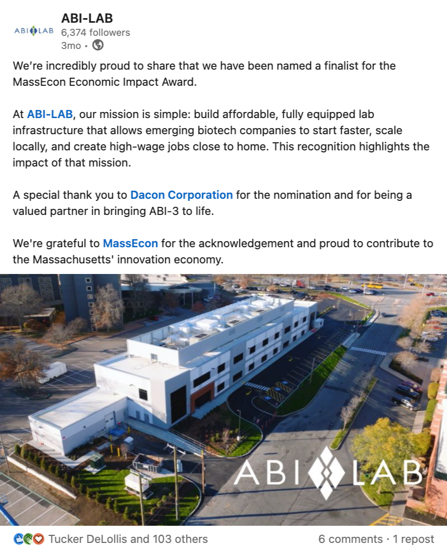 Aerial view of a modern, multi-story laboratory building with white exterior and large windows, surrounded by parking lots and trees, with the ABI-LAB logo overlaid on the lower right corner.