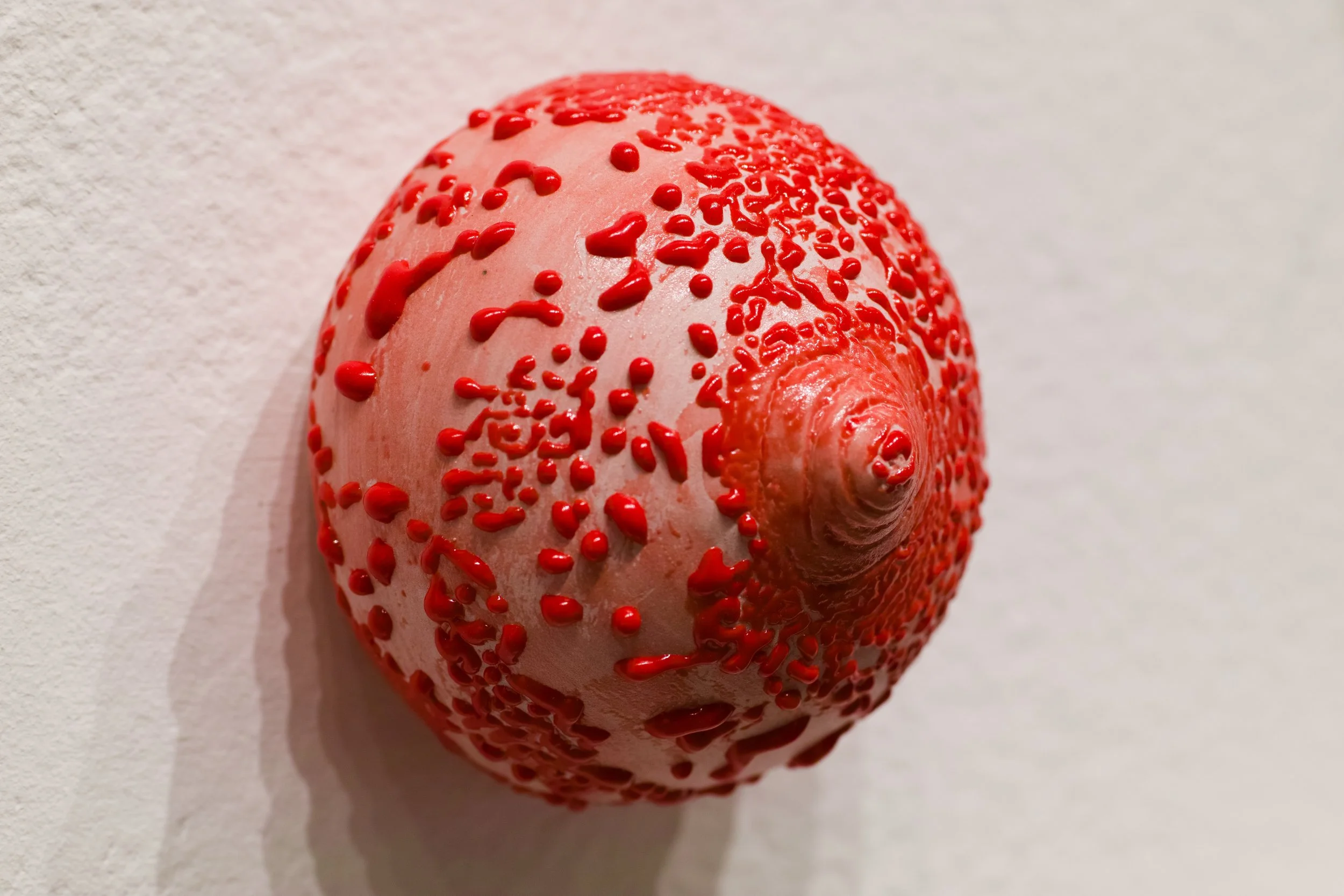 Ceramic wall-mounted breast covered in a goopy red glaze.