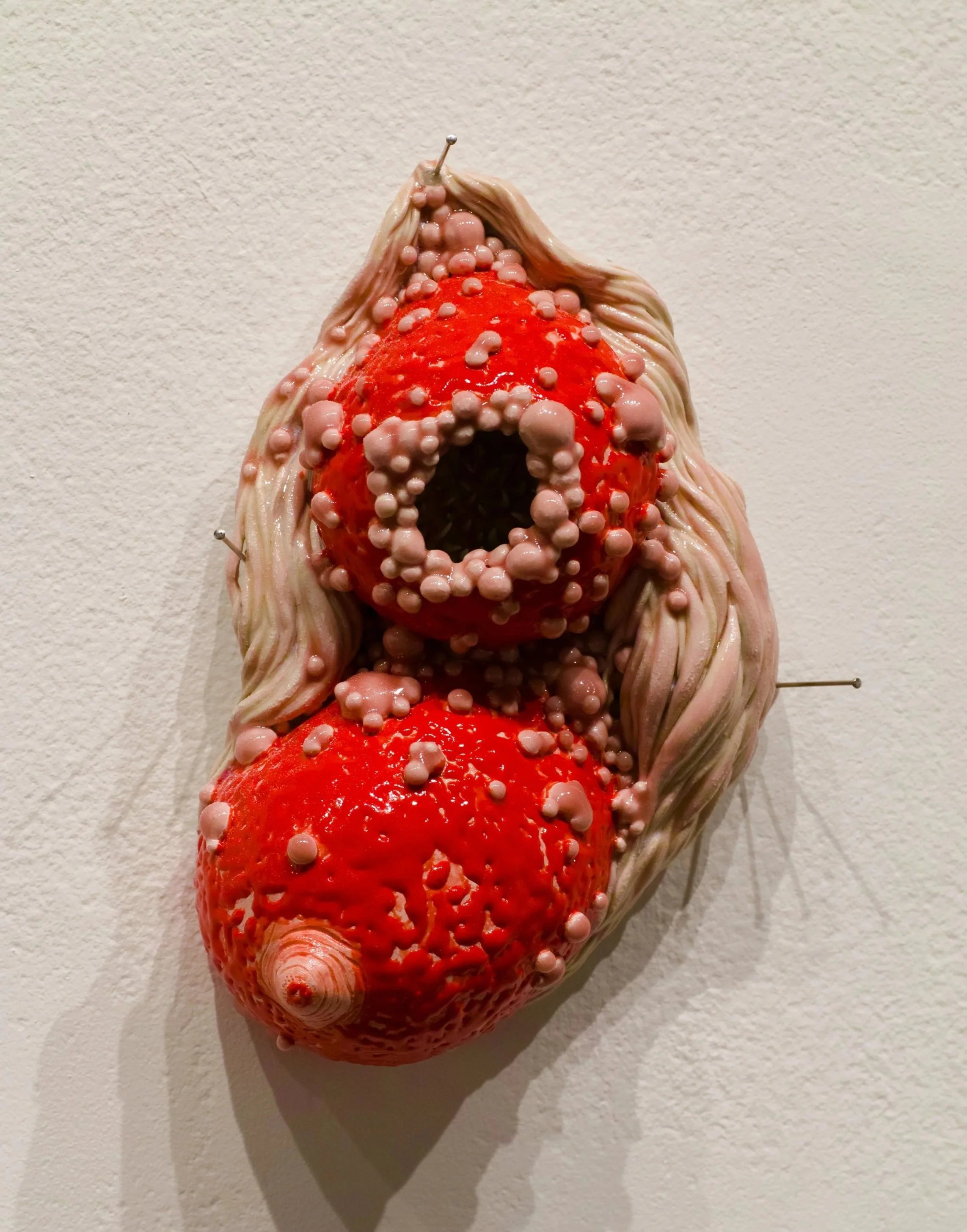 Ceramic wall sculpture of breasts surrounded by abstracted bumpy diseased flesh with a open cavity for viewers to look into.