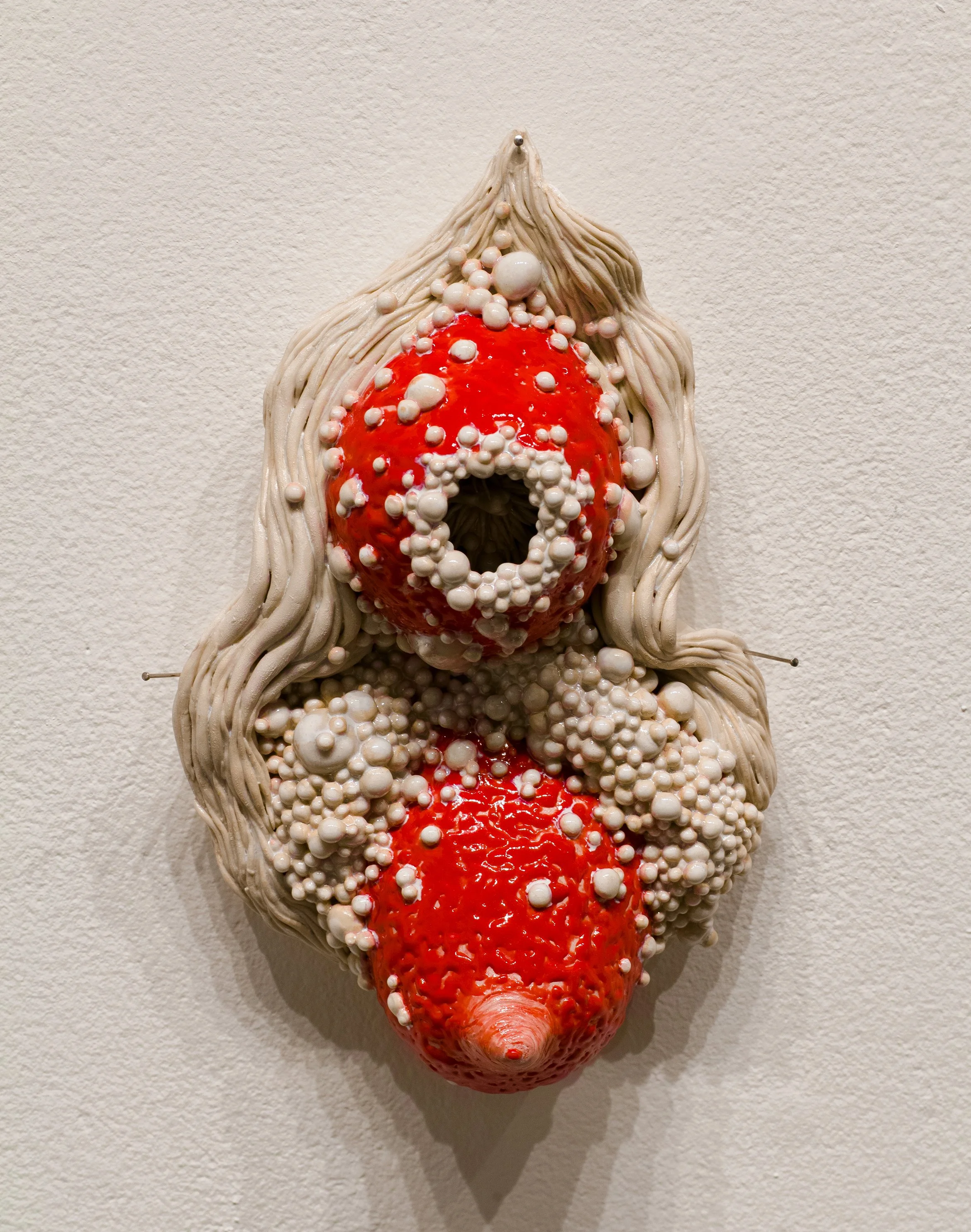 Ceramic wall sculpture of breasts surrounded by abstracted bumpy diseased flesh.